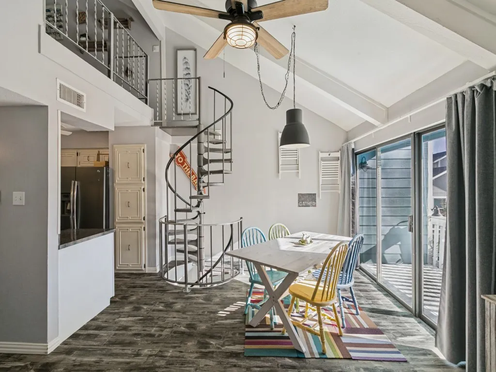 Vaulted ceiling with exposed beams, wood-finish flooring, sliding glass doors, spiral staircase, and an upper-level balcony