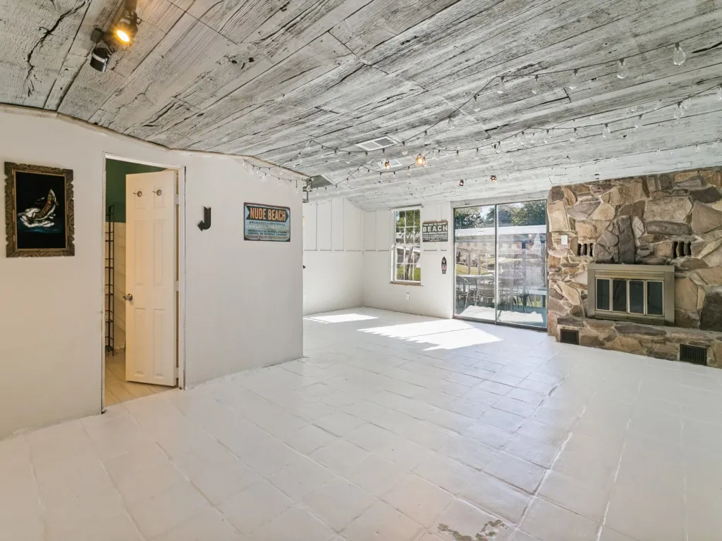 Stone-faced fireplace, distressed wood-finish ceiling, sliding glass doors, white tiled flooring, and recessed lighting