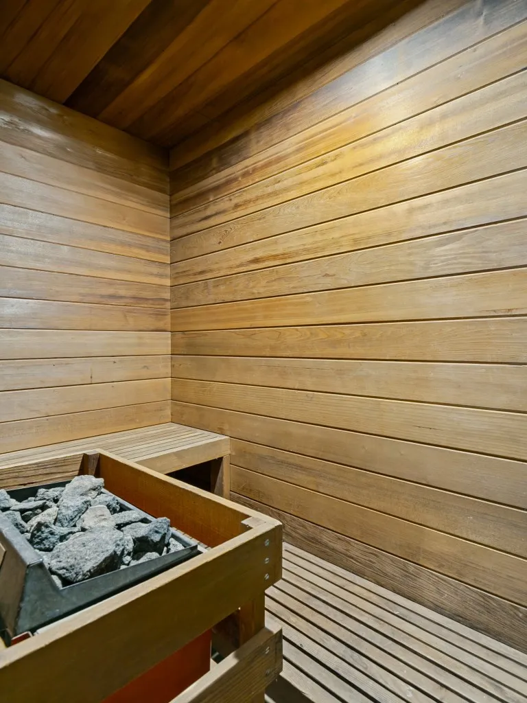 Wood-paneled sauna featuring a built-in bench, slatted wood flooring, and a rock heater