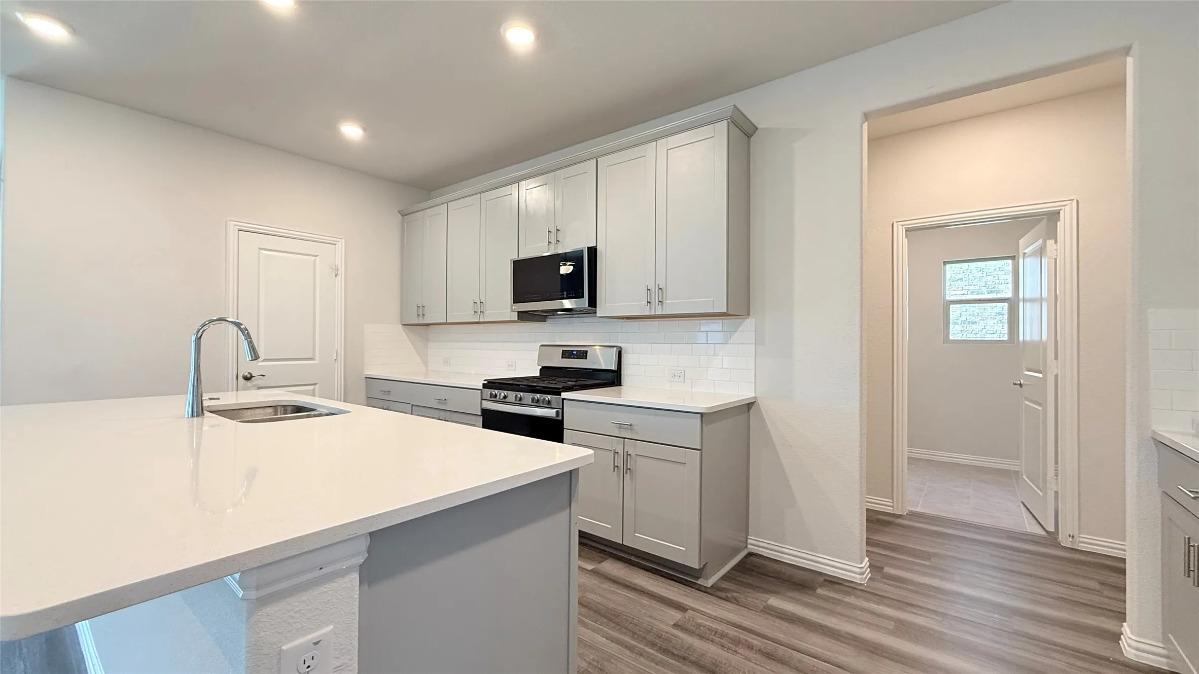 Kitchen featuring light gray cabinetry, white countertops, stainless steel appliances, and wood-finish flooring