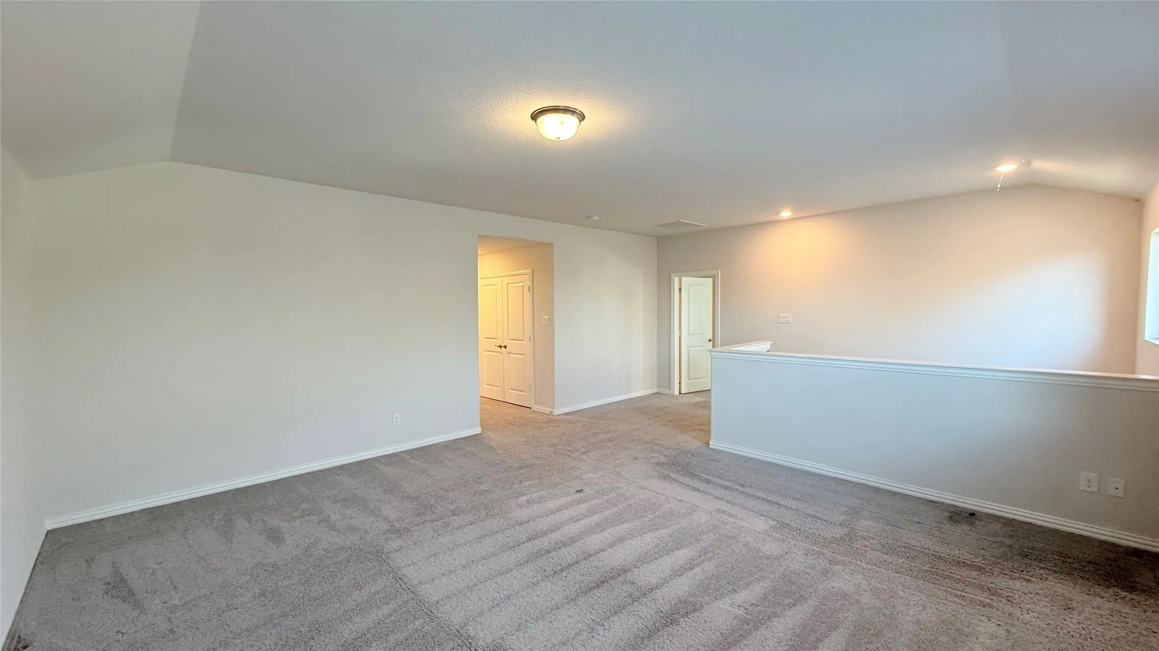 Vaulted ceiling, recessed lighting, neutral tone carpet, half-wall partition, and warm wall color
