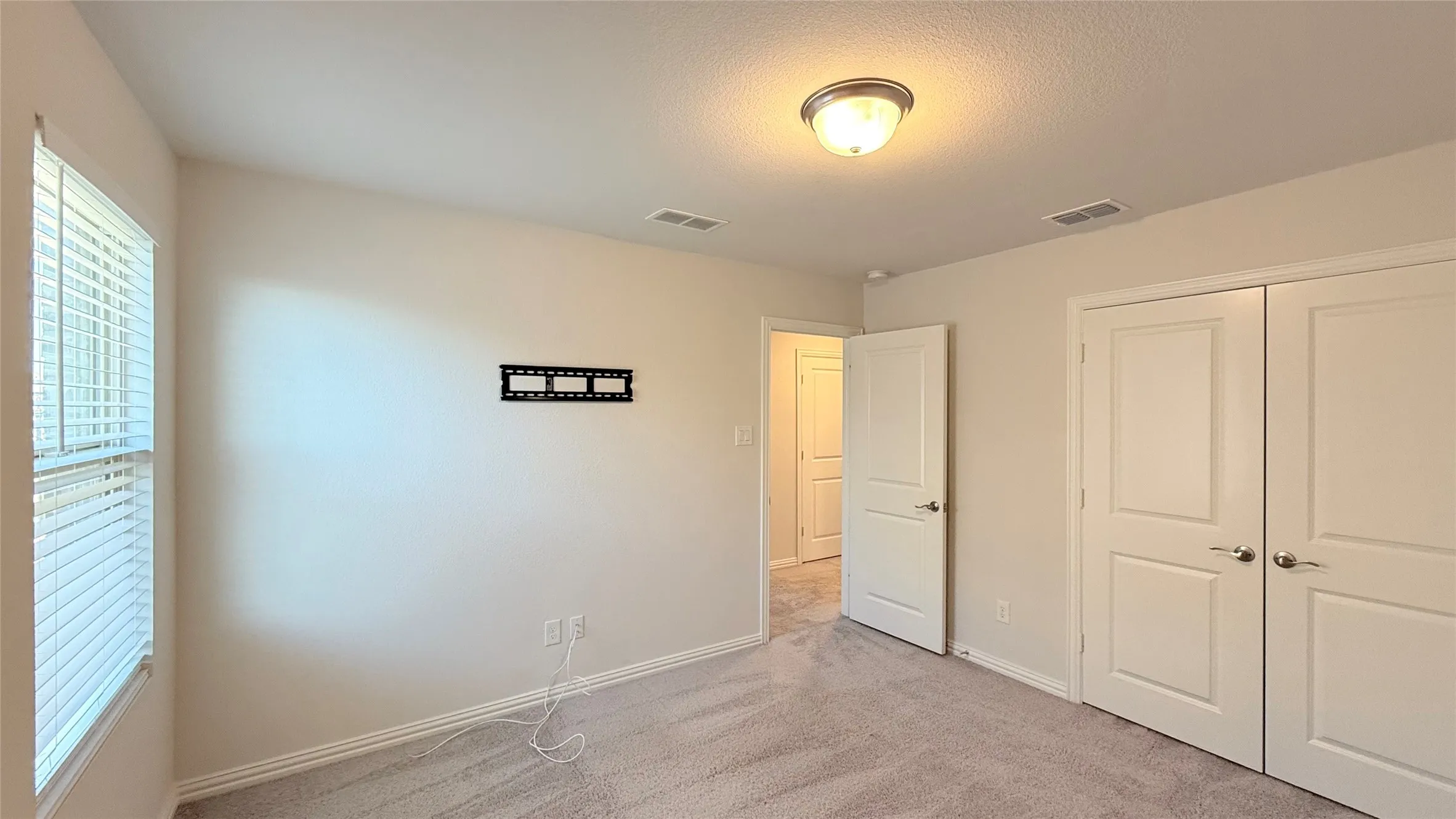 Carpeted room featuring a ceiling-mounted light fixture, louvered window blinds, and paneled doors with satin nickel hardware