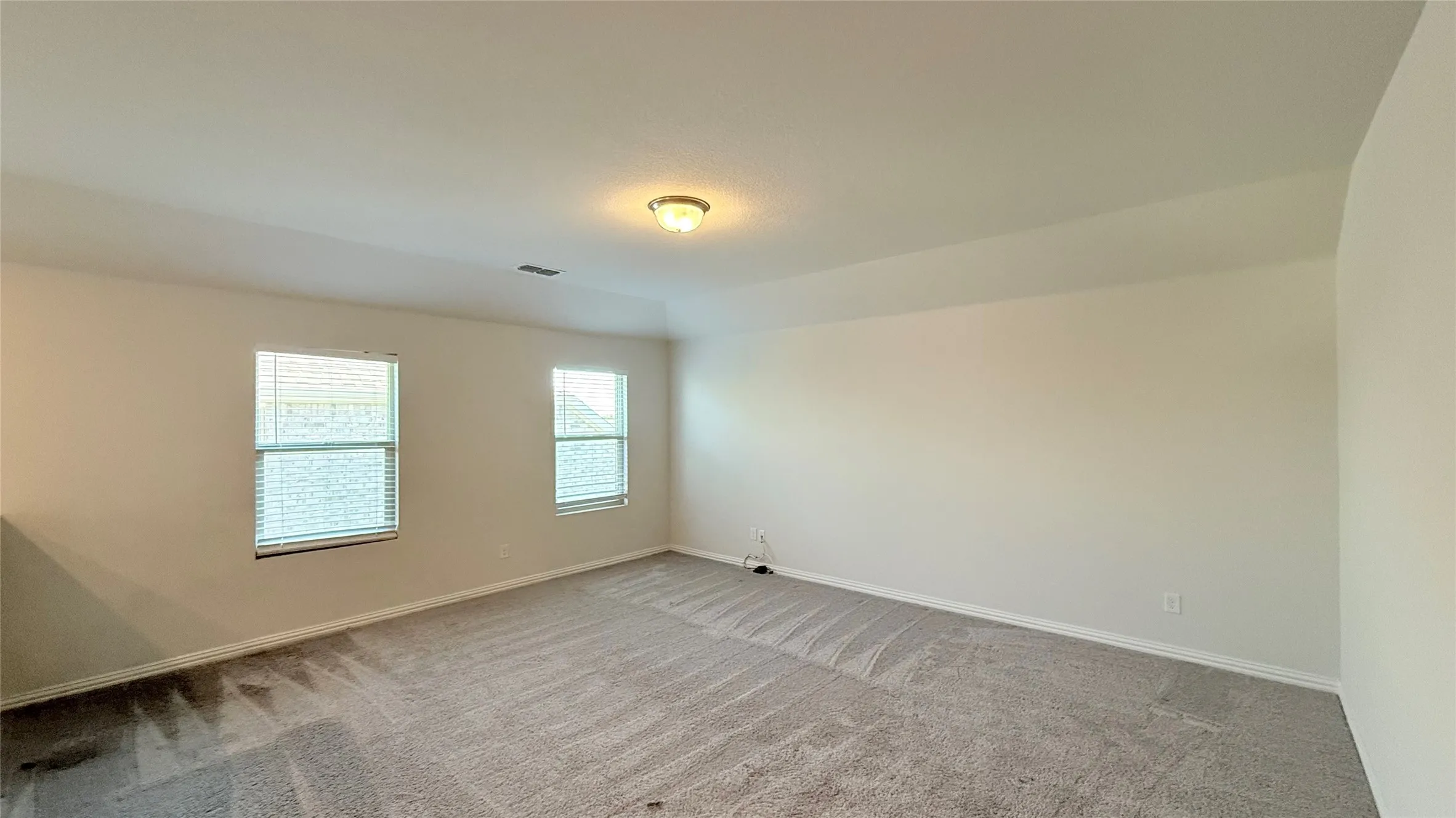 Soft gray carpeting, two windows with blinds, recessed ceiling light, and neutral wall paint