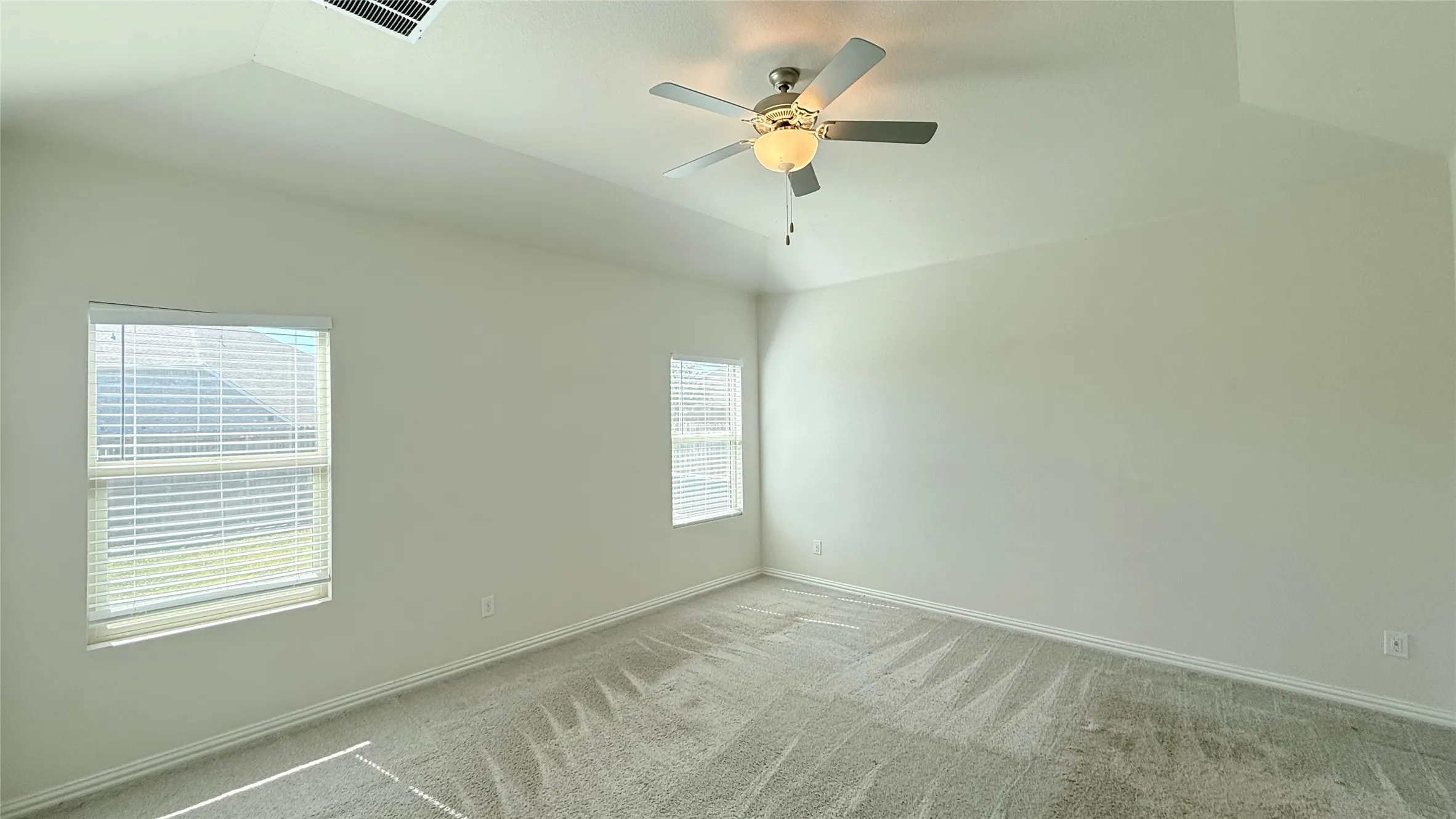 Vaulted ceilings with a ceiling fan, dual windows with blinds, and light-toned carpeting