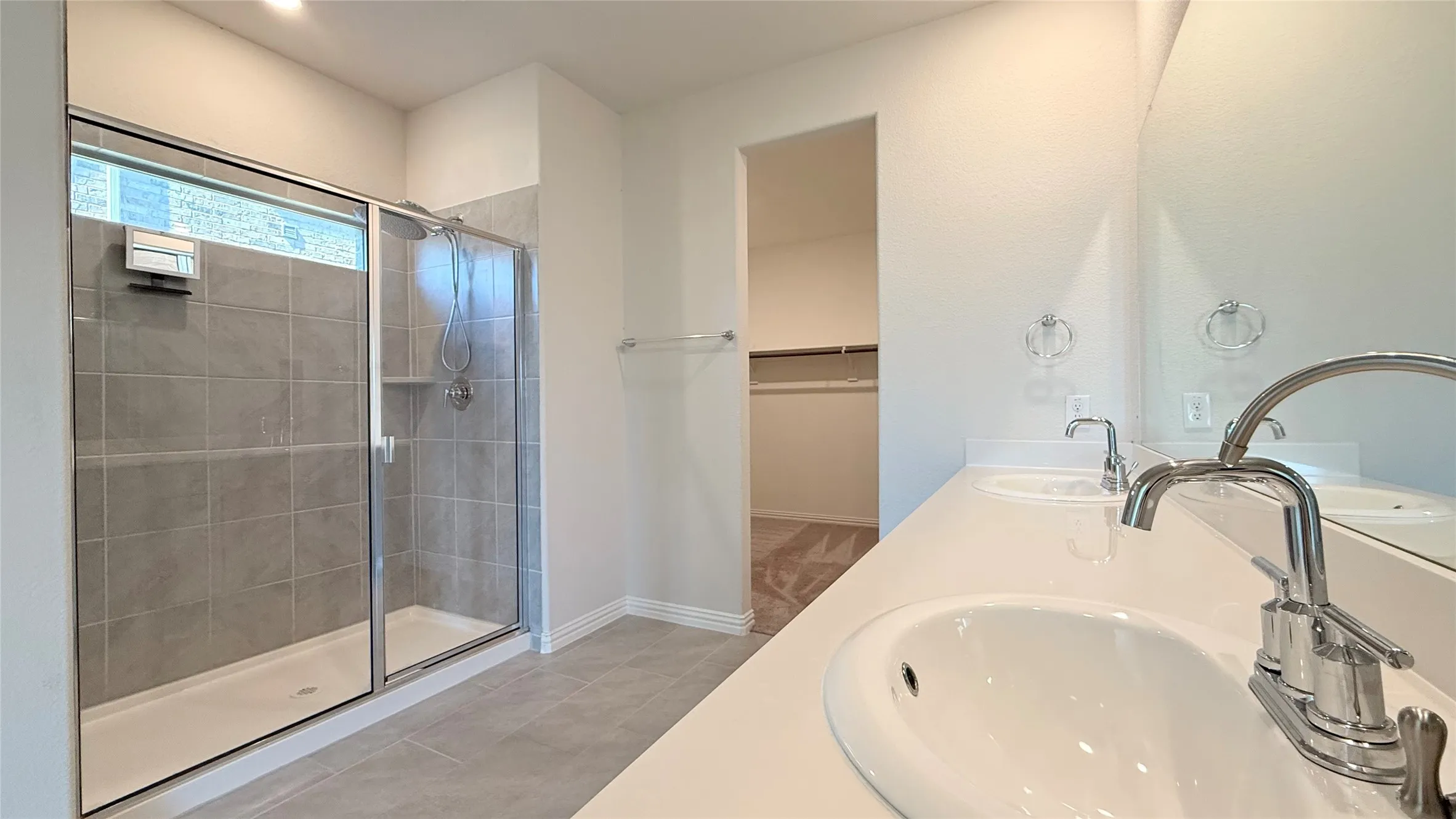 Dual vanity with integrated sinks, expansive counter space, large mirror, glass-enclosed shower, and tiled flooring