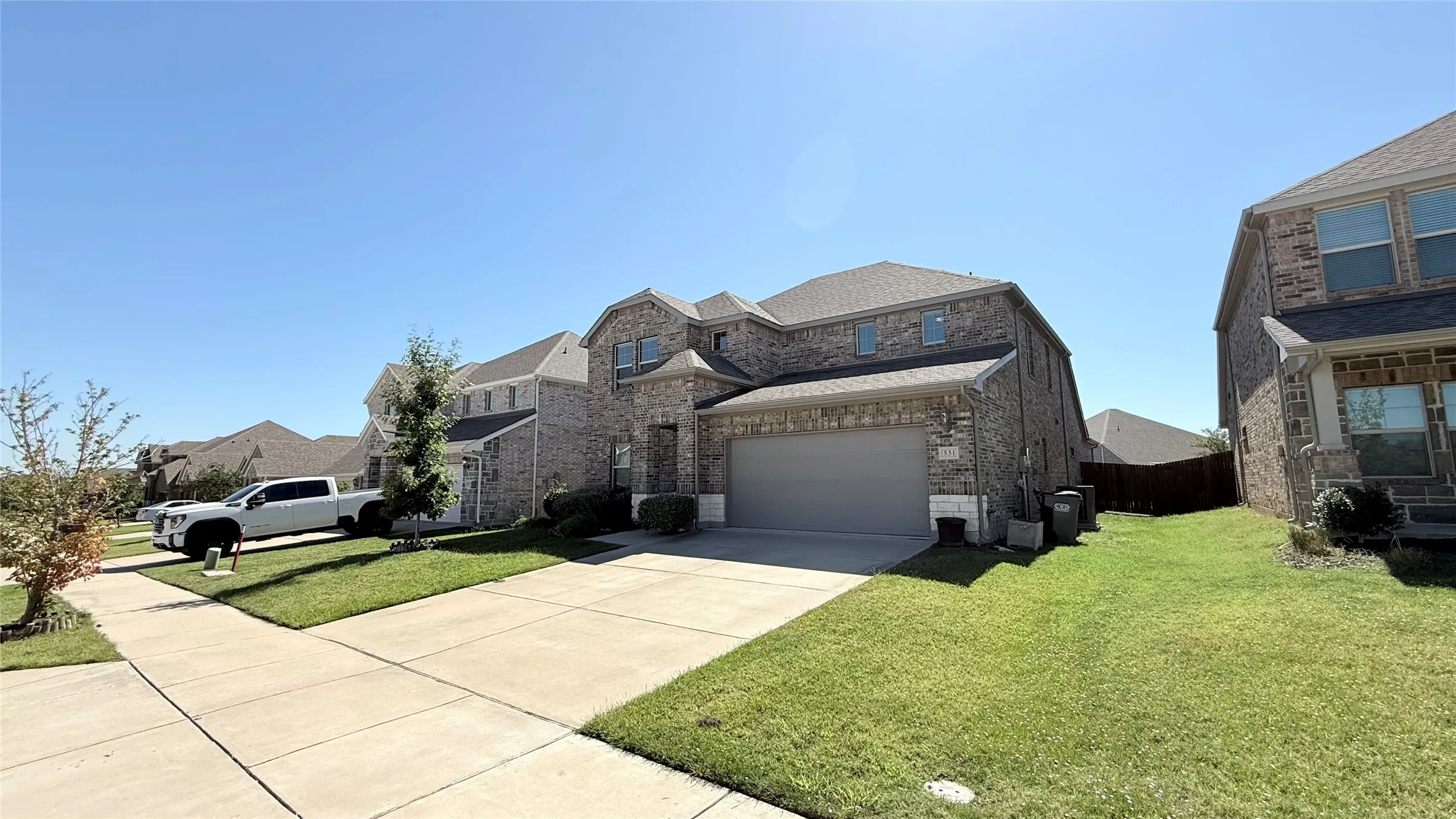 Two-story brick exterior with an attached garage, concrete driveway, and a manicured lawn