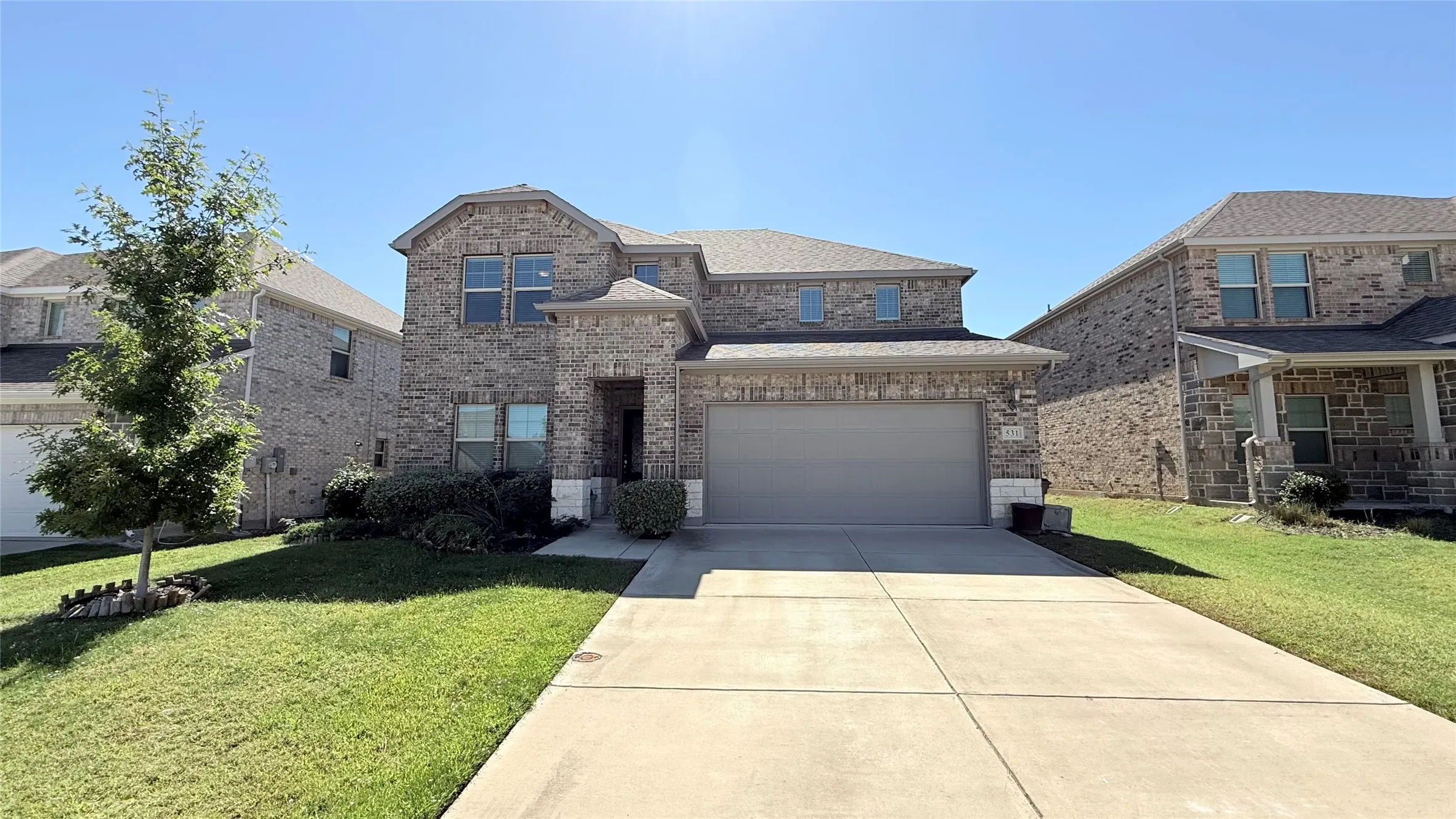 Two-story residential exterior featuring a brick and stone facade, an attached two-car garage, and a concrete driveway