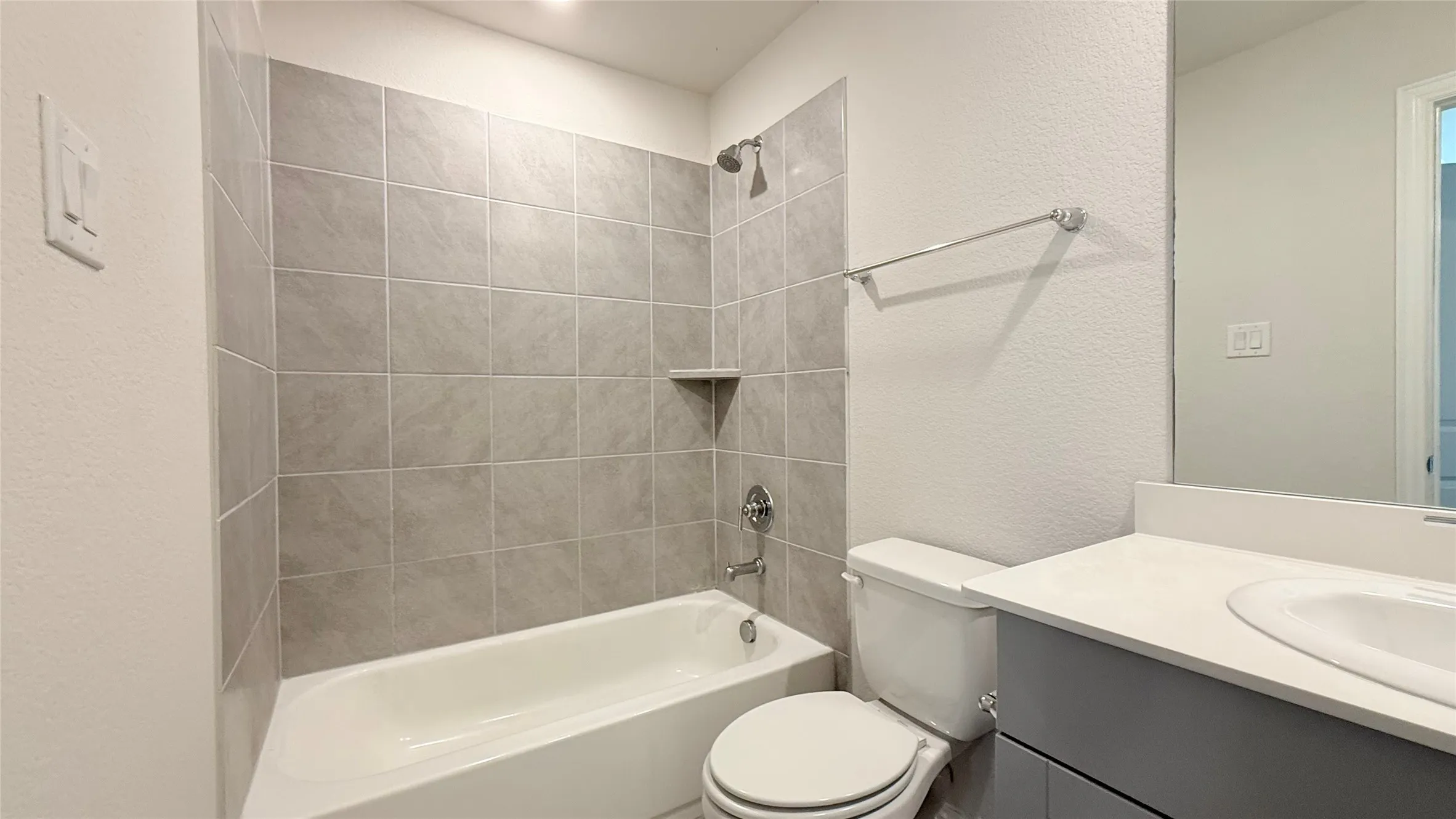 White ceramic bathtub with gray subway tile surround, chrome shower fixtures, and a built-in shower shelf