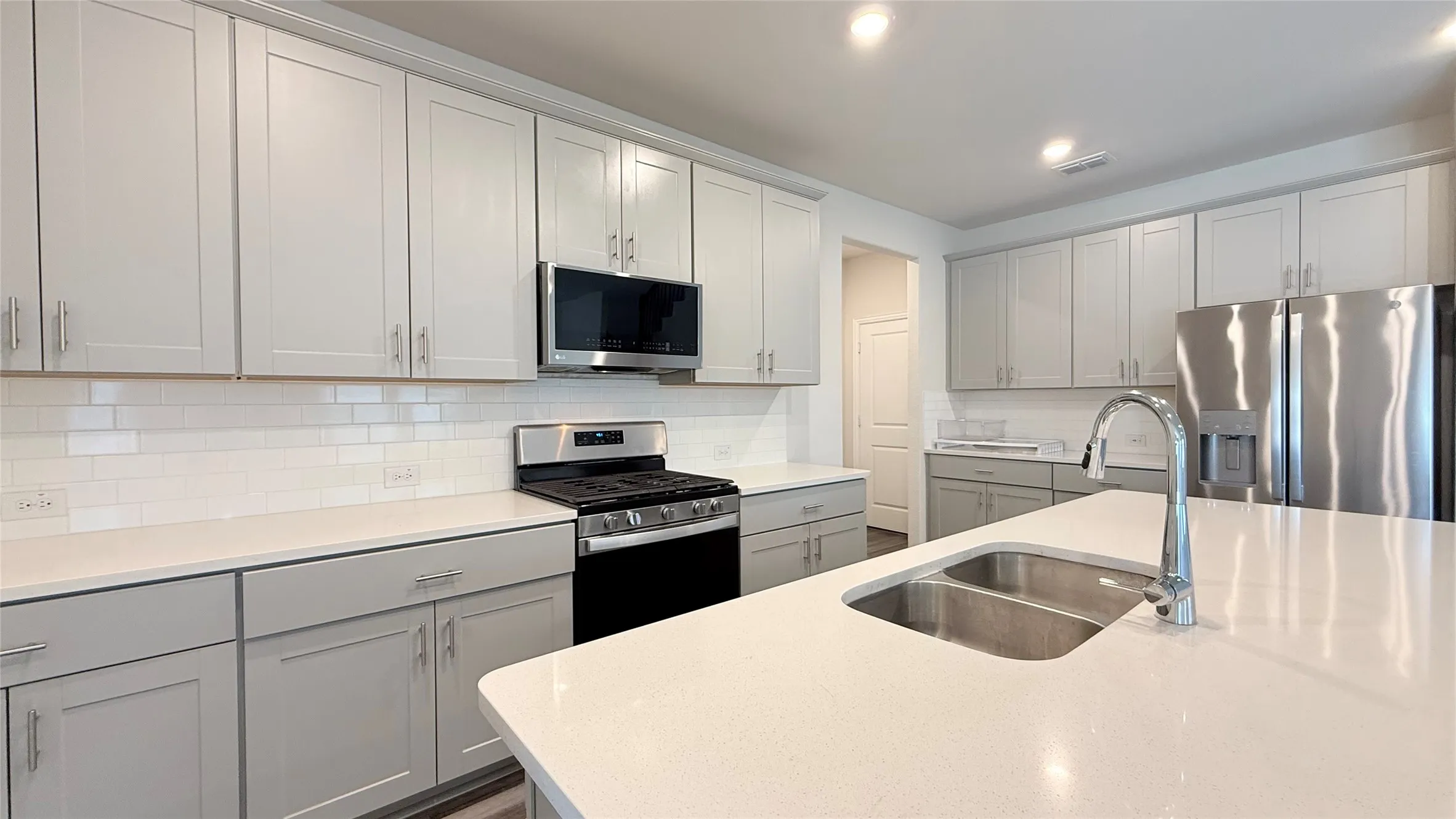 White subway tile backsplash, stainless steel appliances, dual basin sink, light-toned cabinetry, and recessed lighting