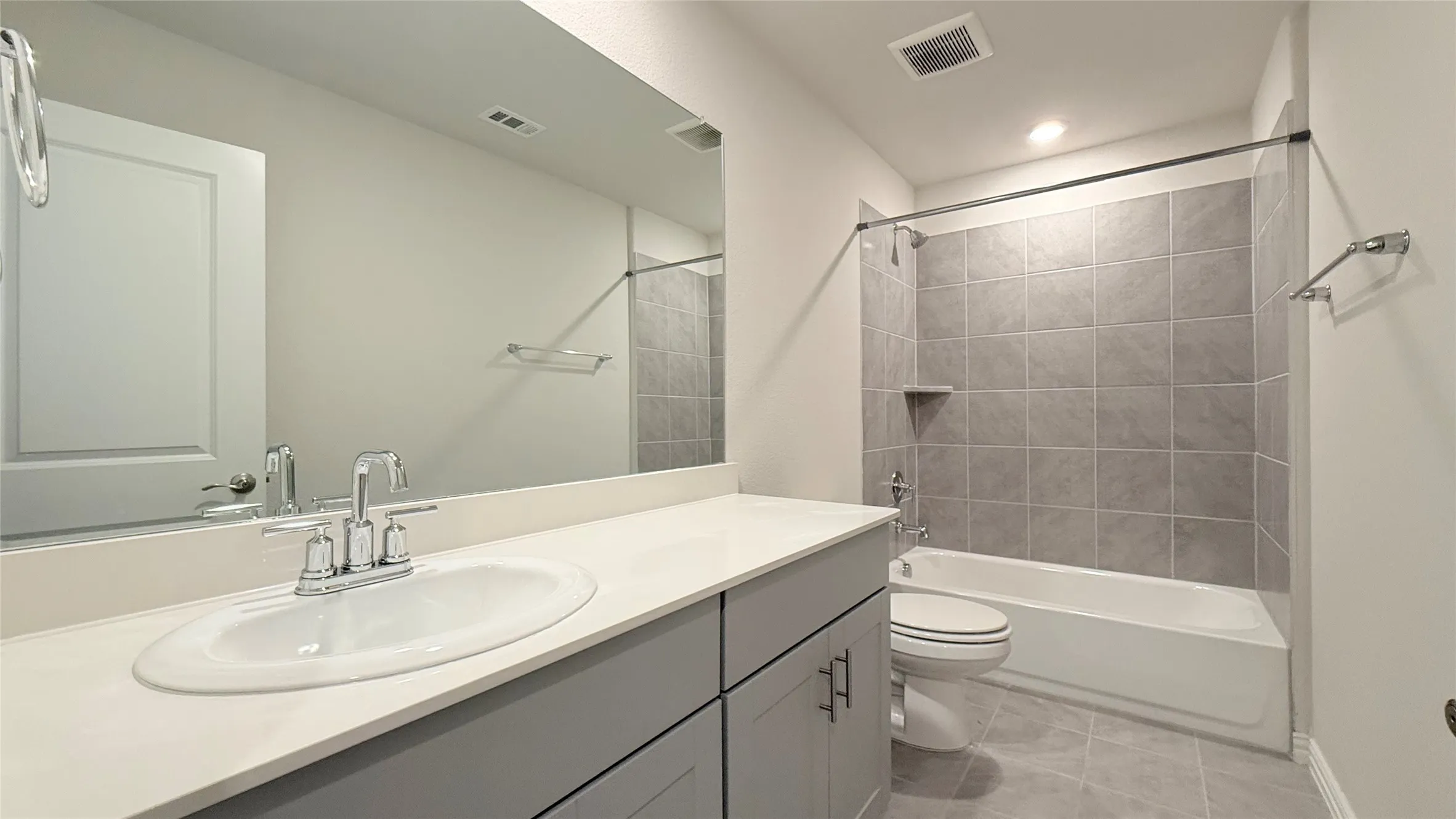 Bathroom featuring a vanity with a white countertop and undermount sink, a large wall-mounted mirror, a tiled shower-tub combination with a built-in niche, and tiled flooring