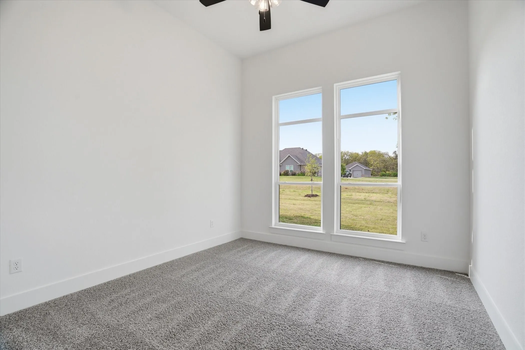 Vaulted ceiling room featuring twin windows, plush gray carpeting, and a ceiling fan