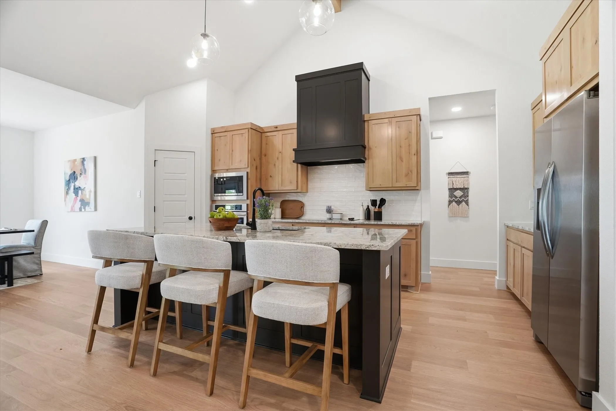 Kitchen featuring a large island with stone countertops, stainless steel appliances, wood-finish flooring, a tile backsplash, and light wood cabinetry