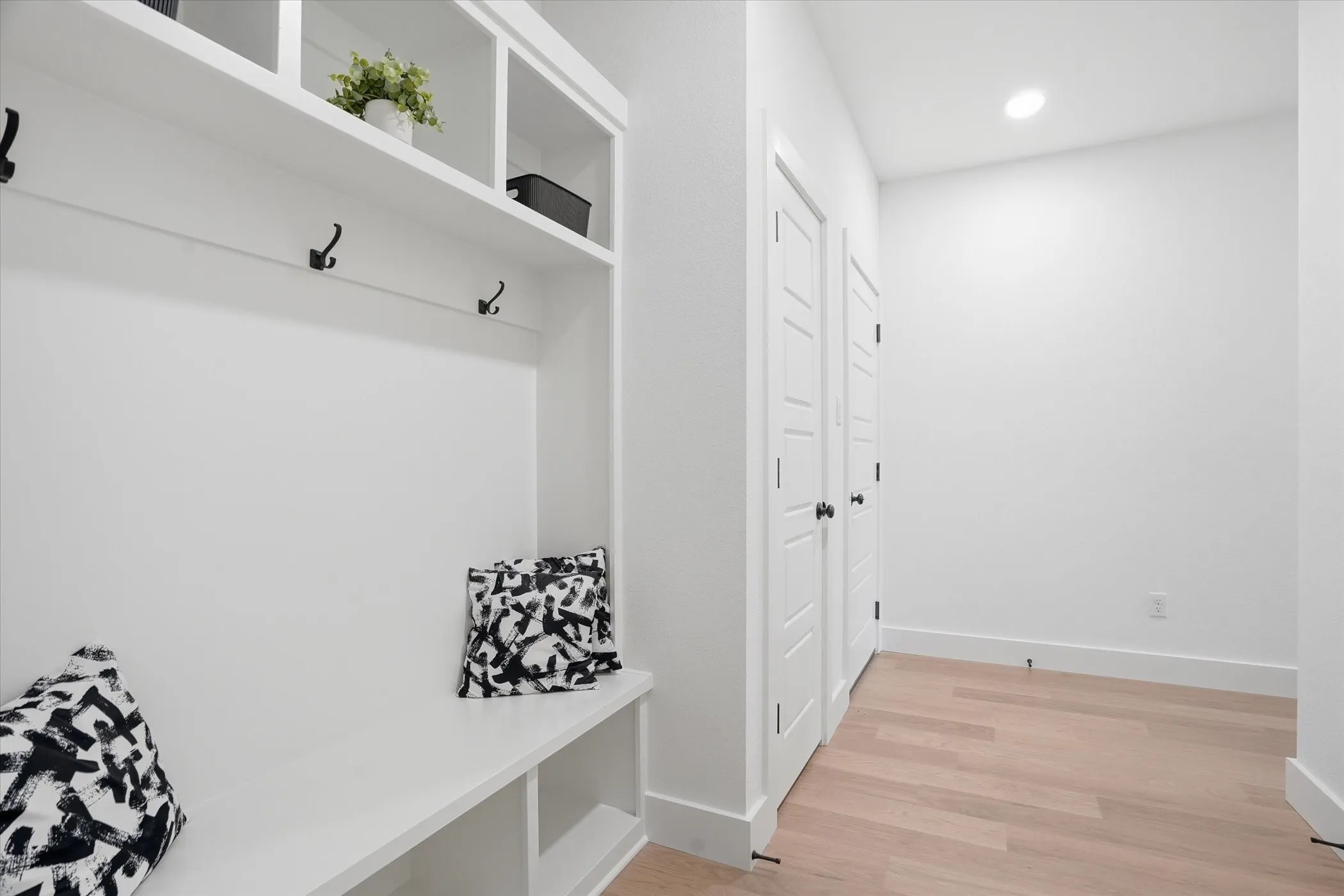 Entry area featuring light wood-finish flooring, recessed lighting, built-in shelving, storage cubbies, and multiple paneled doors