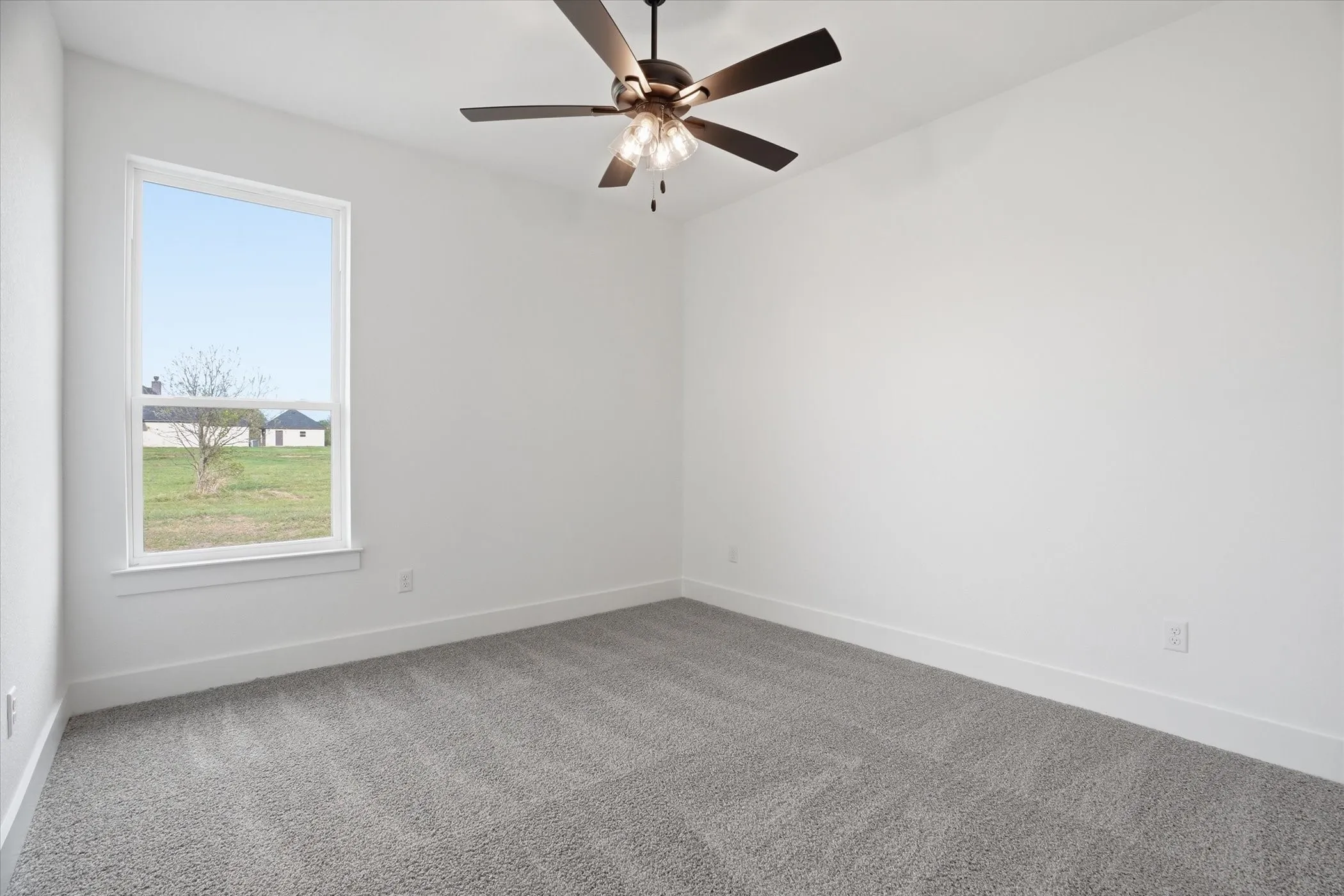 Neutral wall color, grey carpet, ceiling fan with integrated lighting, and a single pane window