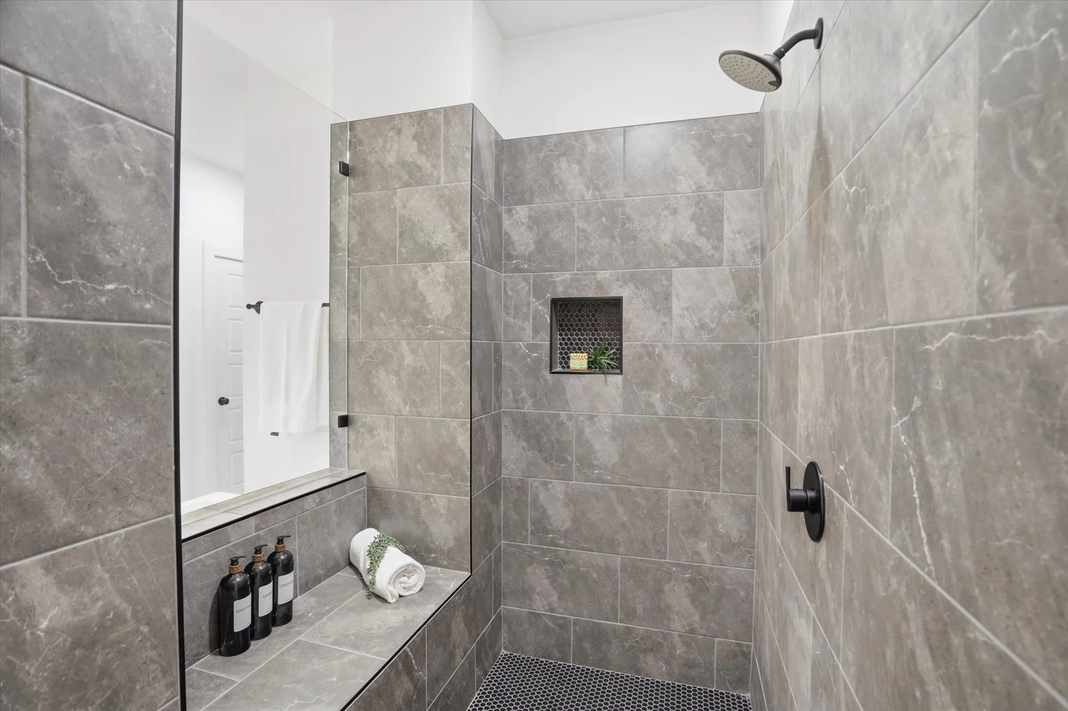 Tiled shower with a built-in bench, recessed niche, matte black fixtures, and a glass partition
