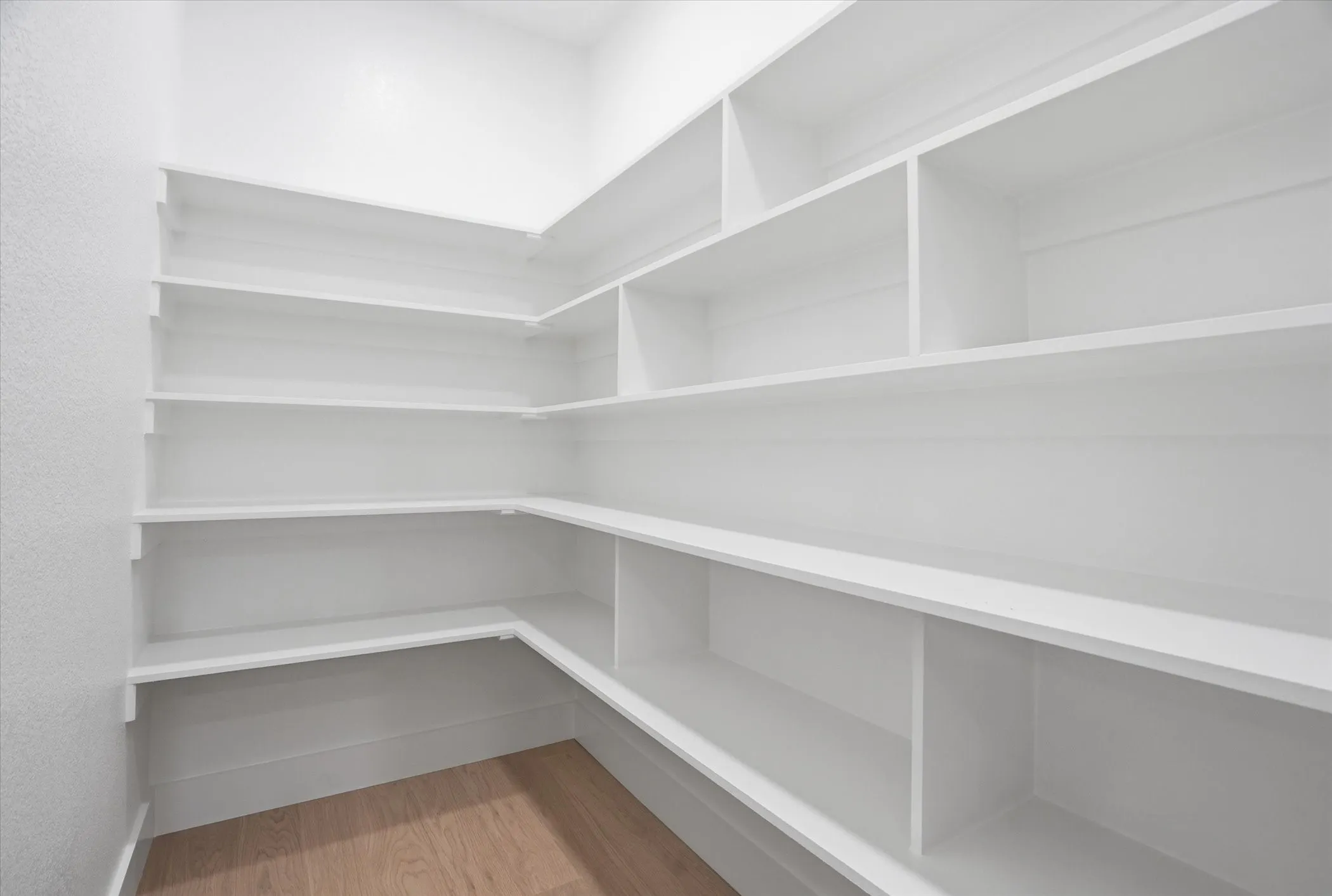 Expansive pantry featuring wrap-around shelving, multiple storage compartments, and wood-finish flooring