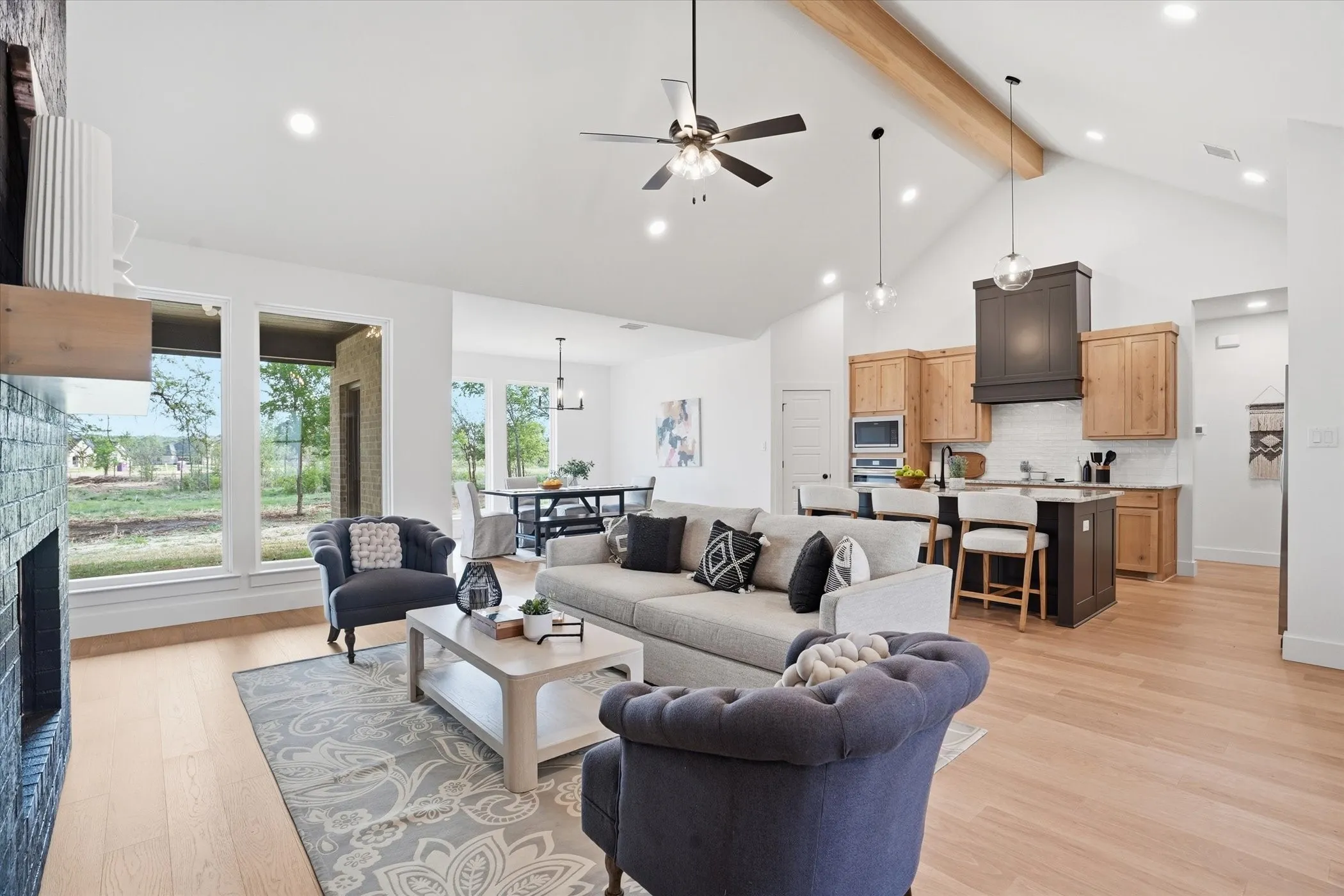 Vaulted ceilings with wood beam accent, recessed lighting, wood-finish flooring, built-in fireplace, and a kitchen island with seating