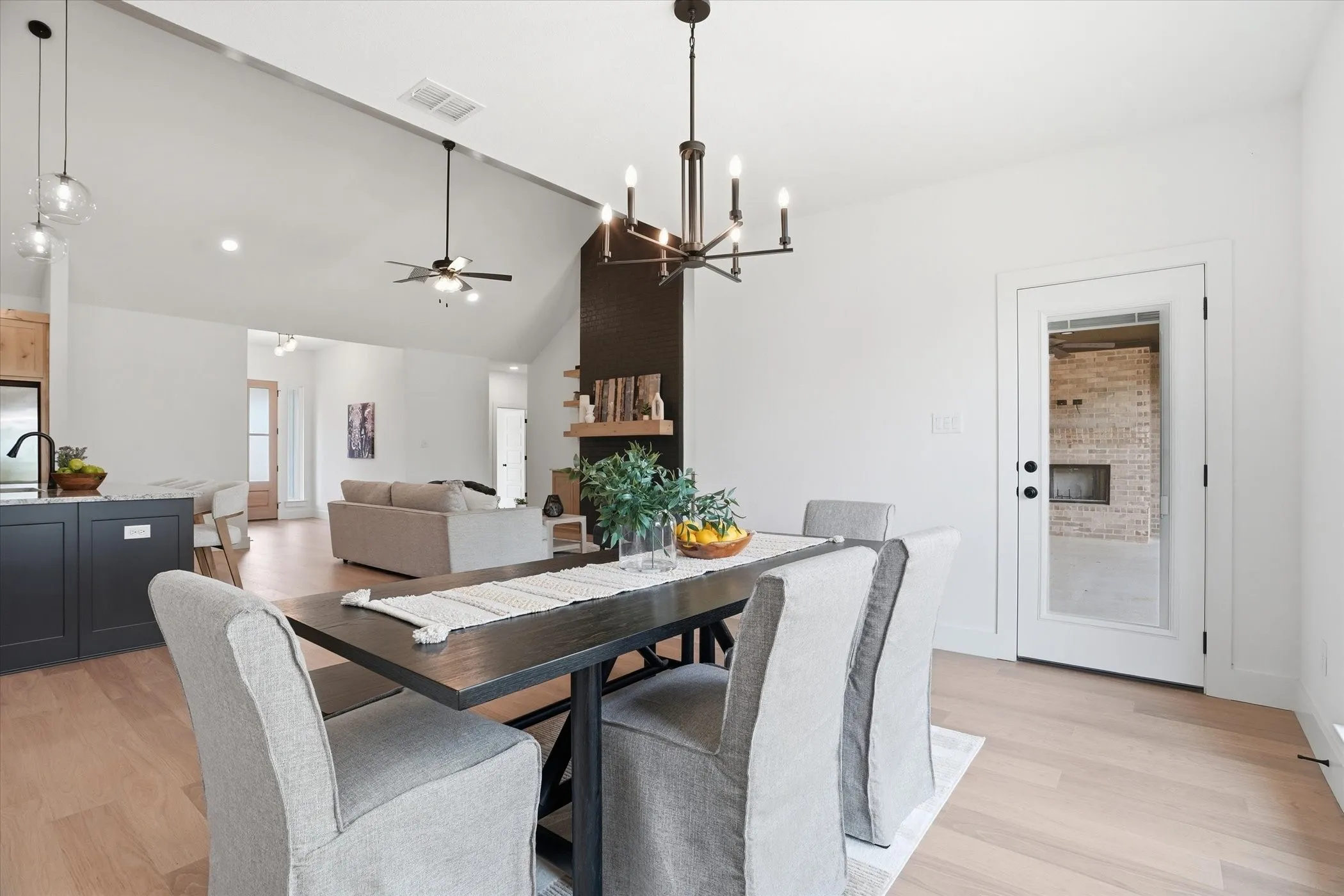 Vaulted ceiling, wood-finish flooring, white walls, dark-finish dining table, and a glass-panel door