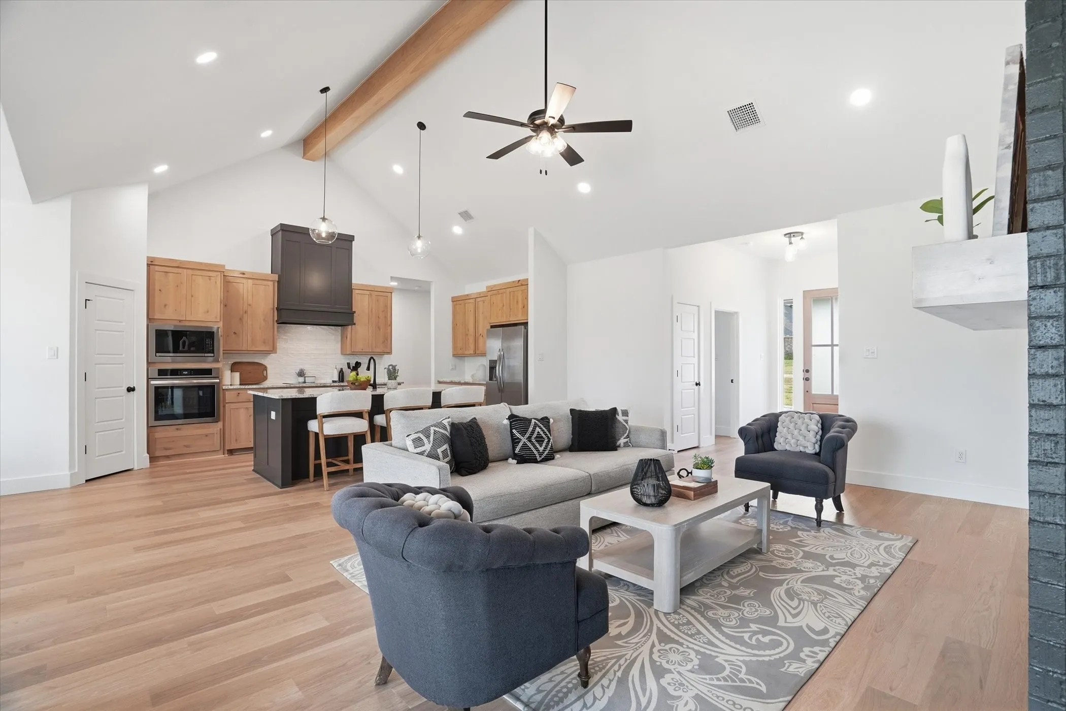Vaulted ceiling with exposed wood beam, recessed lighting, wood-finish flooring, built-in kitchen appliances, and a kitchen island with seating