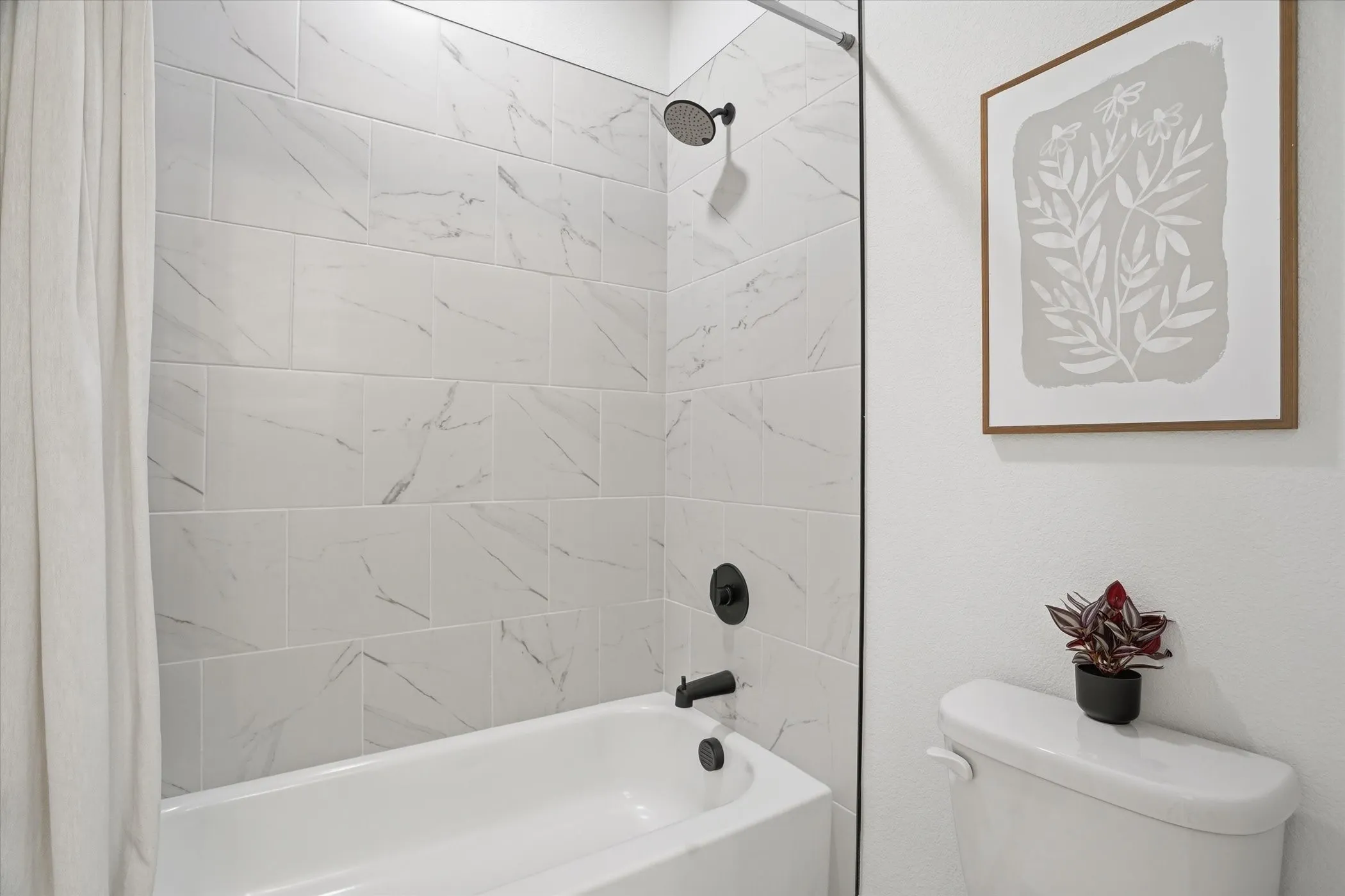 Bathtub with matte black fixtures, white tile surround, and white walls