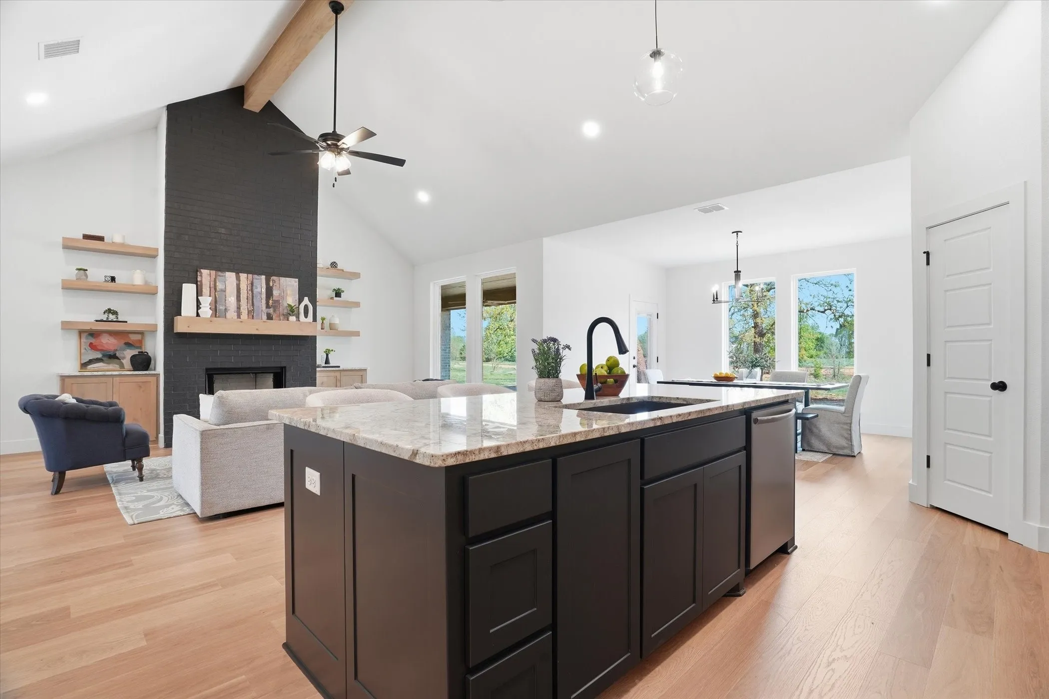 Open-concept living space featuring vaulted ceilings, a central kitchen island with a built-in sink, stainless steel appliances, and wood-finish flooring