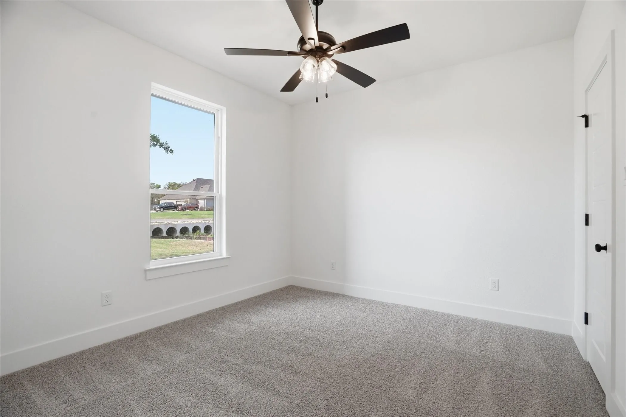 White walls, gray carpet flooring, a window with white trim, a ceiling fan with integrated lighting, and a white door with black hardware