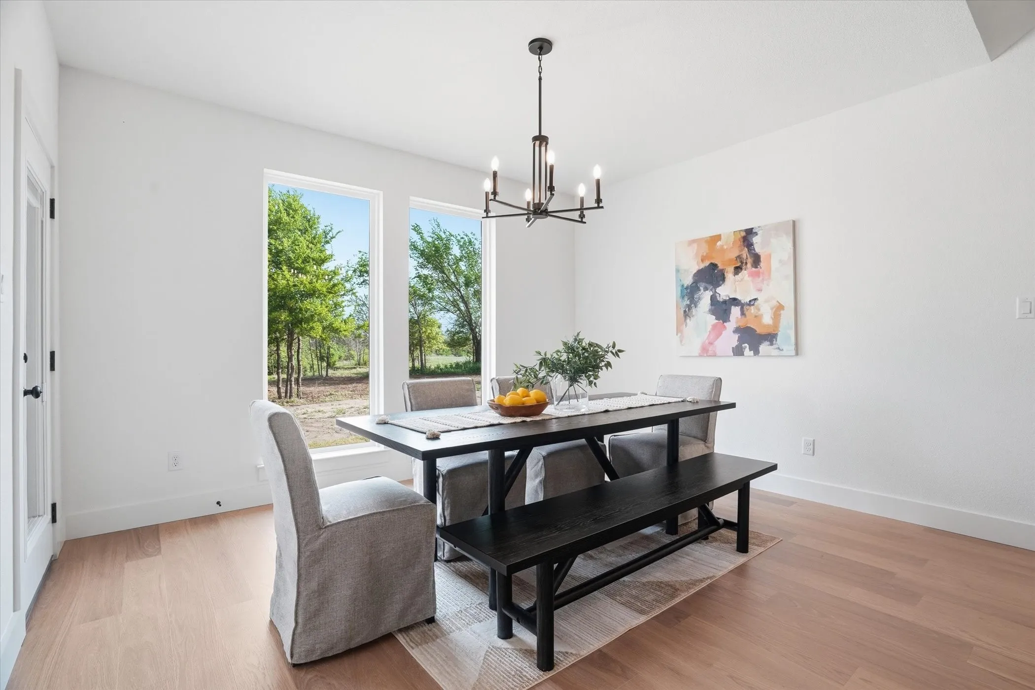 Light wood-finish flooring, white walls, two large picture windows, and a modern chandelier
