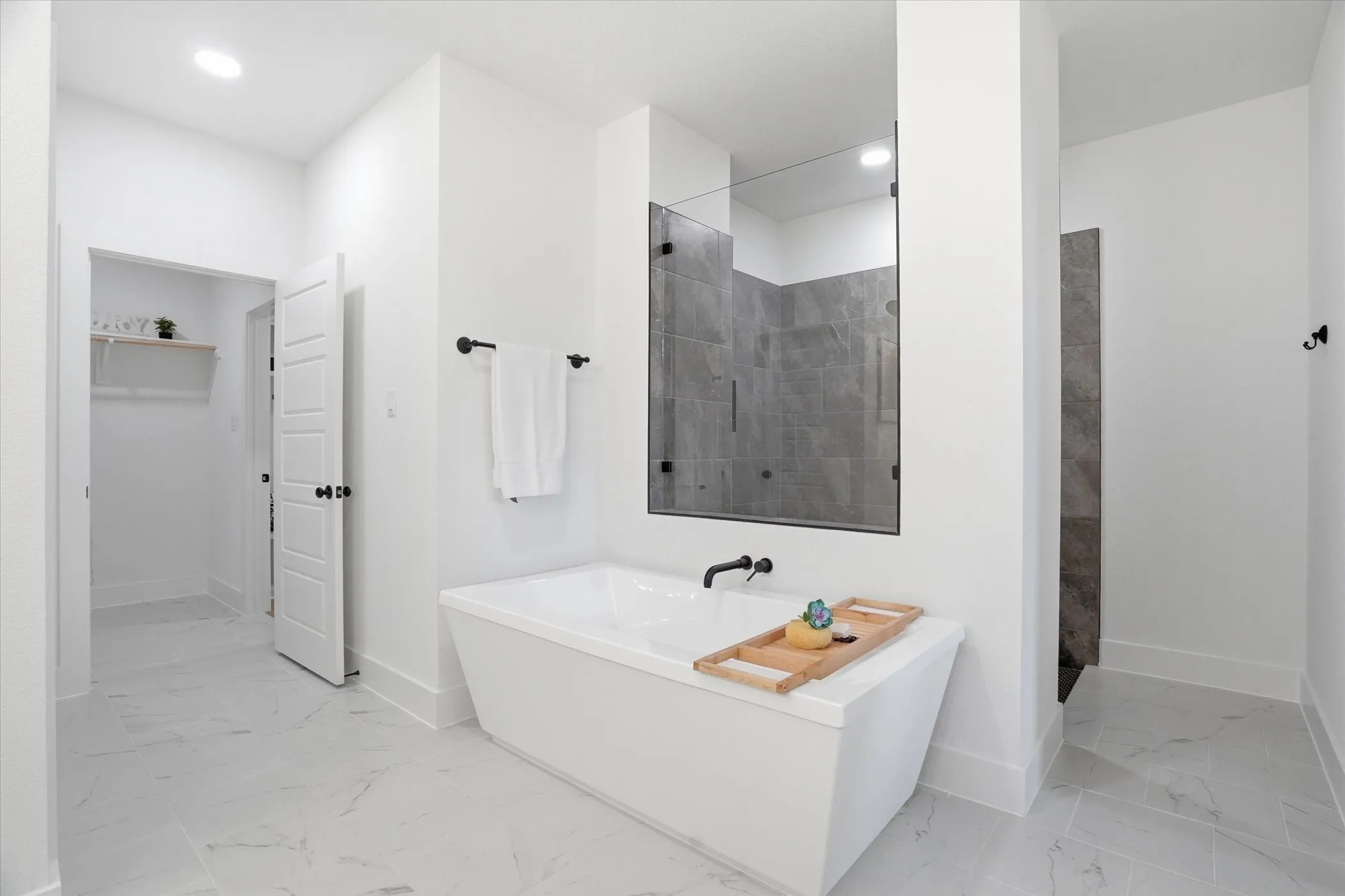 Freestanding soaking tub, large glass-enclosed shower with dark tile, white panel doors, recessed lighting, and light-toned tile flooring