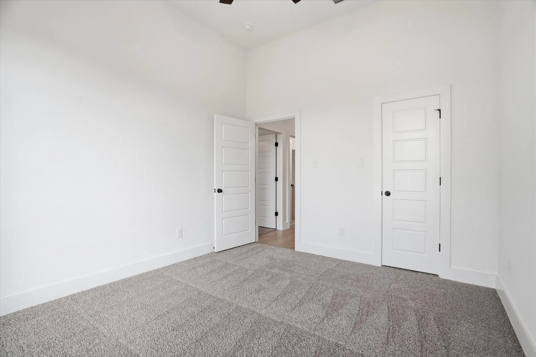Vaulted ceiling, clean white walls, gray carpet, contemporary panel doors, and black hardware