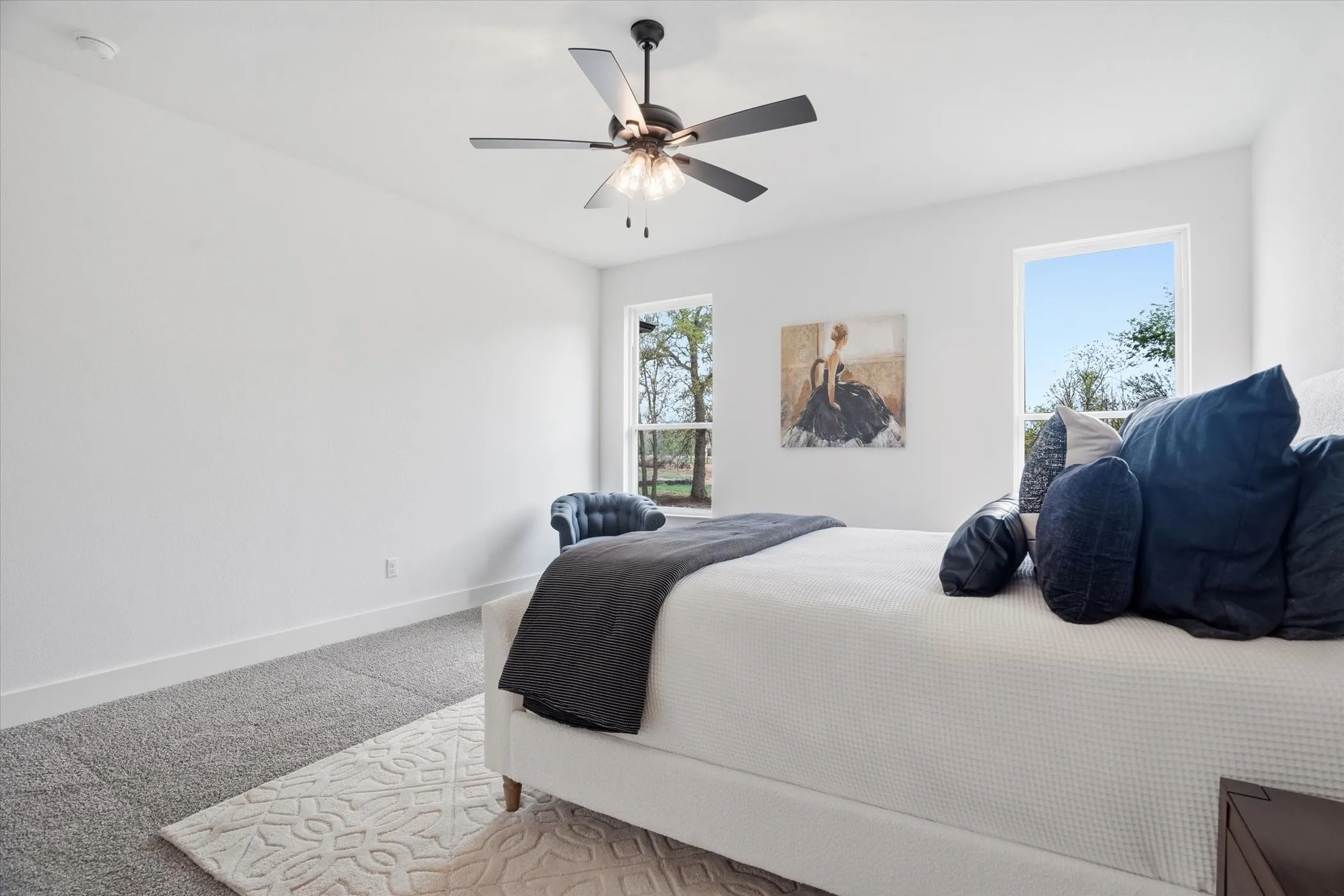 Bright primary bedroom featuring a ceiling fan with integrated lighting, large windows flooding the space with natural light, wood-finish flooring, and neutral wall finishes