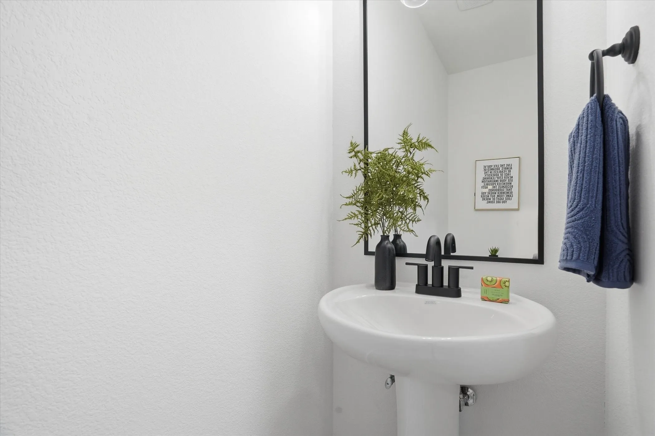 Pedestal sink with a matte black faucet and rectangular framed mirror