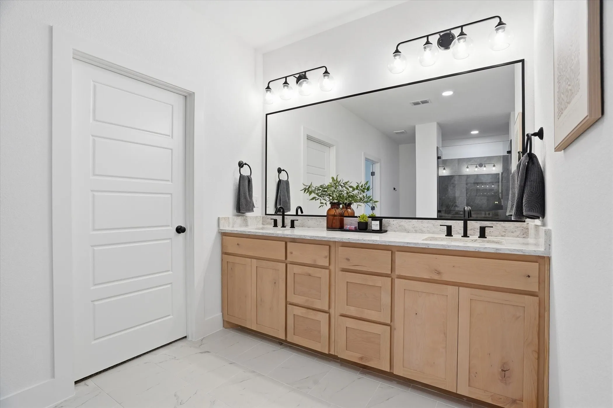 Dual vanity with light wood-finish cabinetry, light-toned countertop, and matte black fixtures