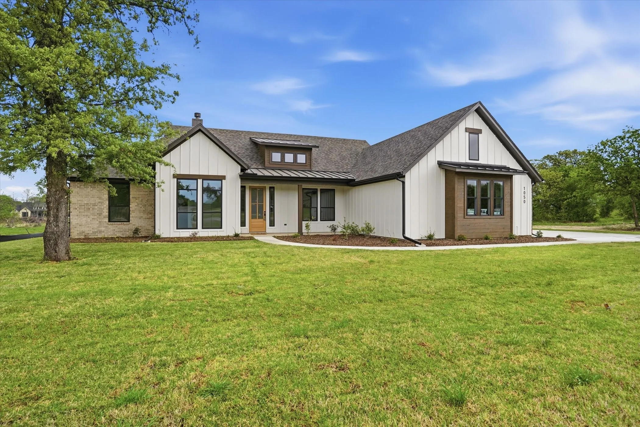 Modern farmhouse exterior with white board and batten siding, brick accents, dark-framed windows, and a wood entry door