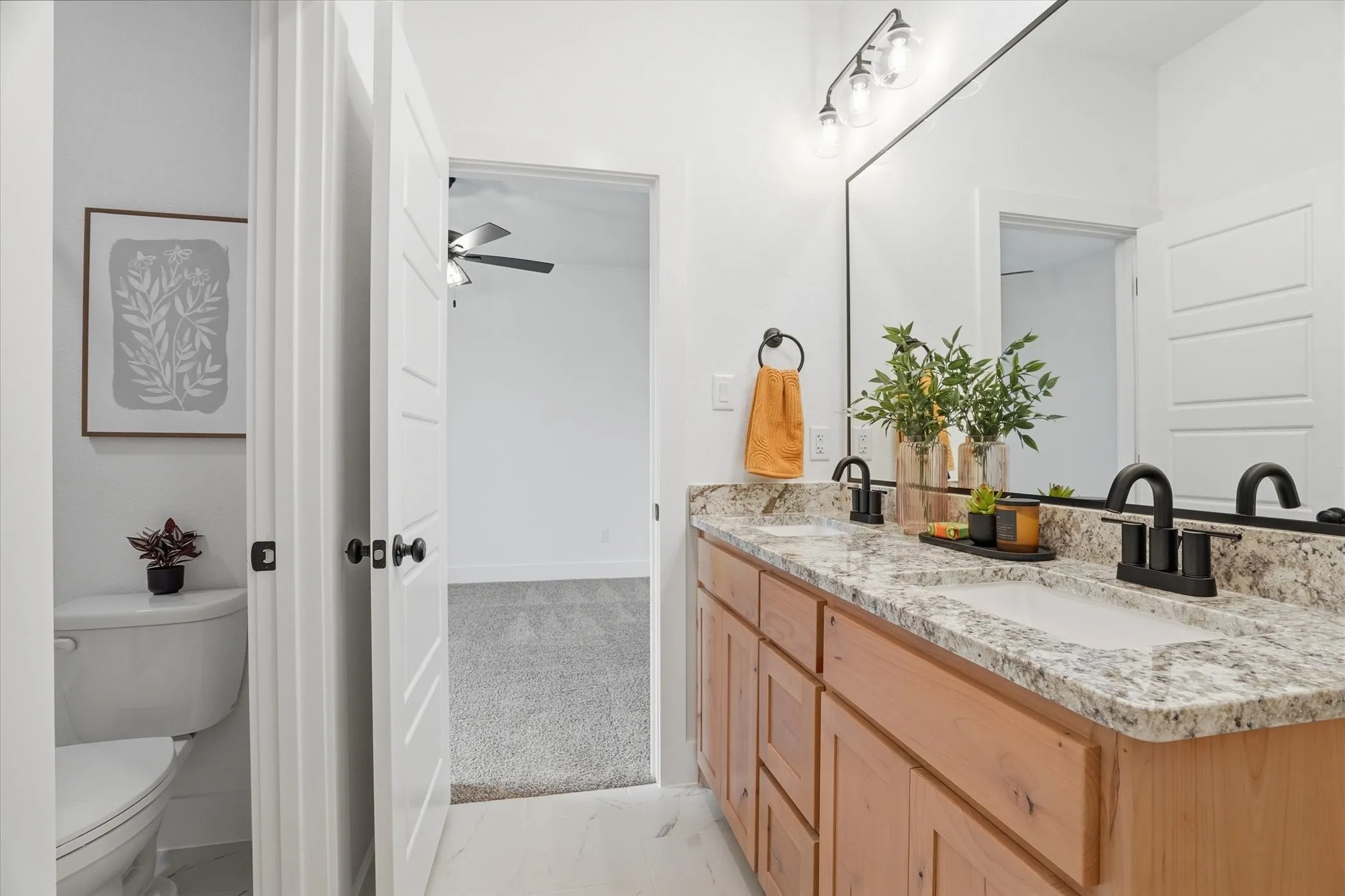 Dual sink vanity with light wood cabinetry, granite-style countertop, and matte black fixtures