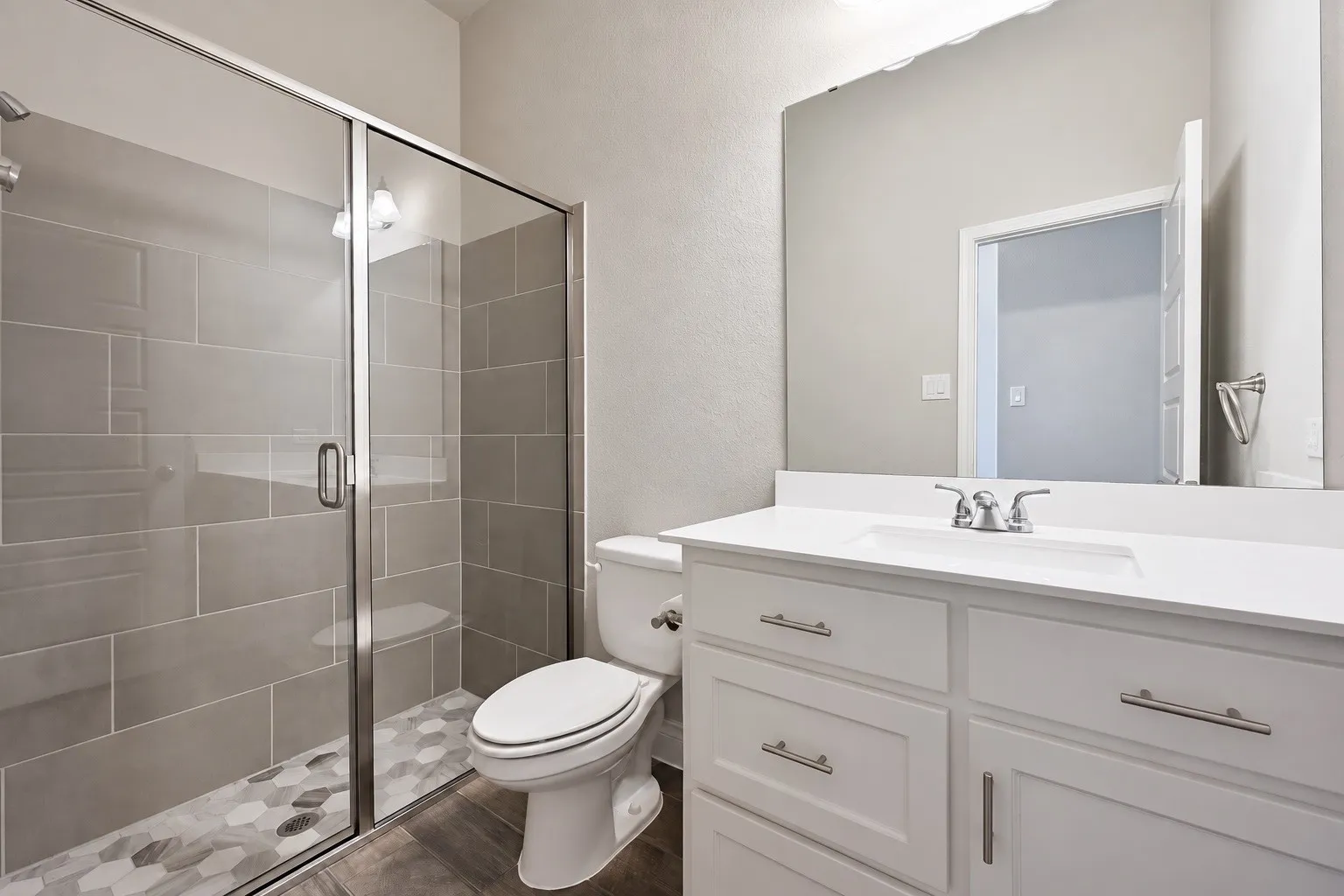 Walk-in shower with clear glass enclosure, gray subway tile surround, and hexagonal floor tile