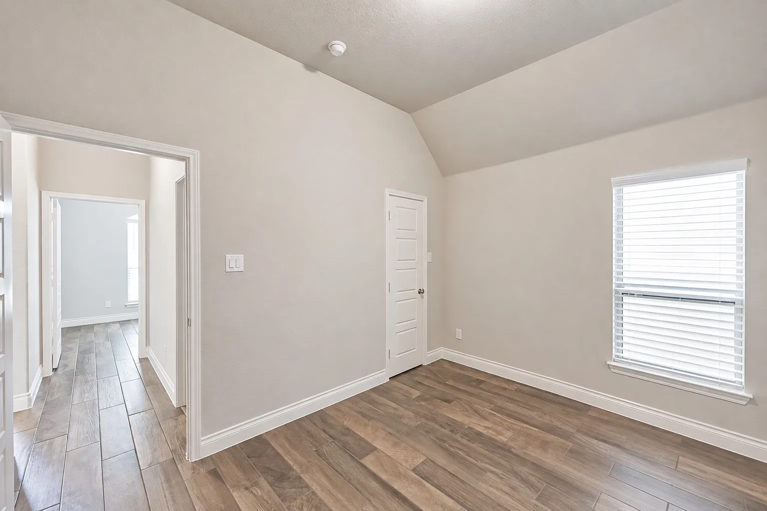 Vaulted ceiling with a flush-mount light fixture, wood-look tile flooring, and a window with blinds