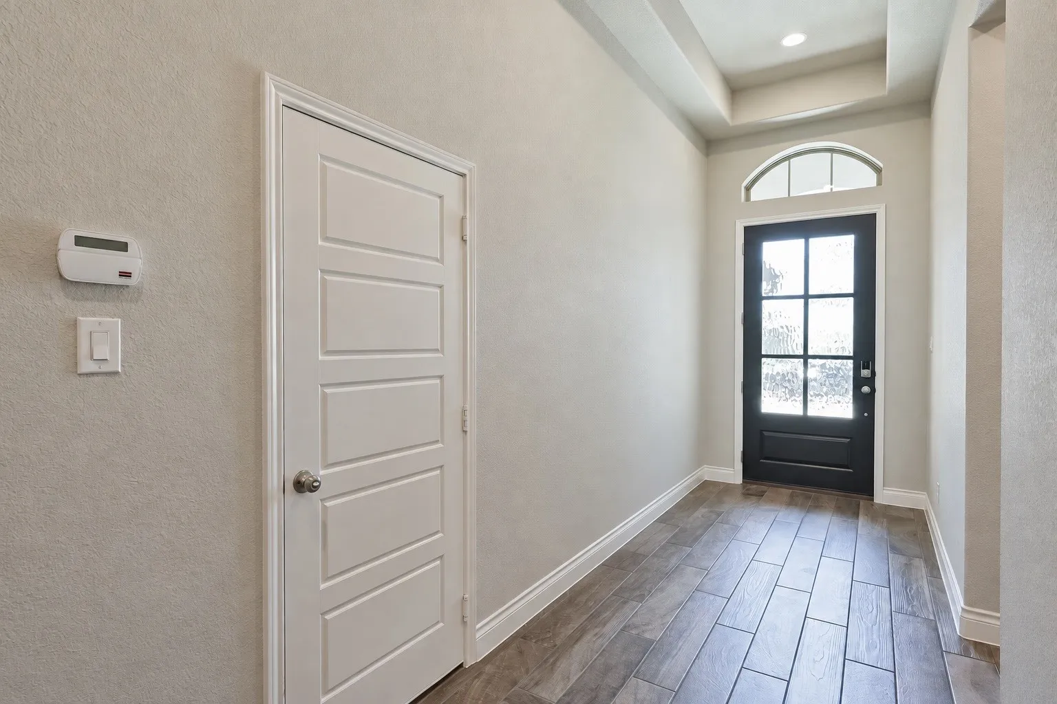 Entryway featuring wood-finish tile flooring and a black front door with an arched transom window