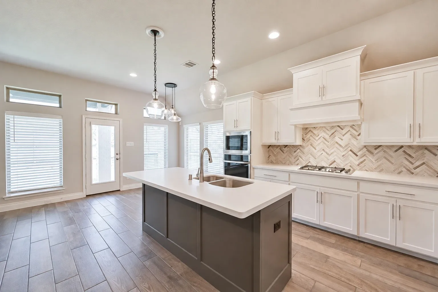 Kitchen featuring a center island with sink, white shaker-style cabinetry, herringbone tile backsplash, integrated stainless steel appliances, and wood-finish flooring
