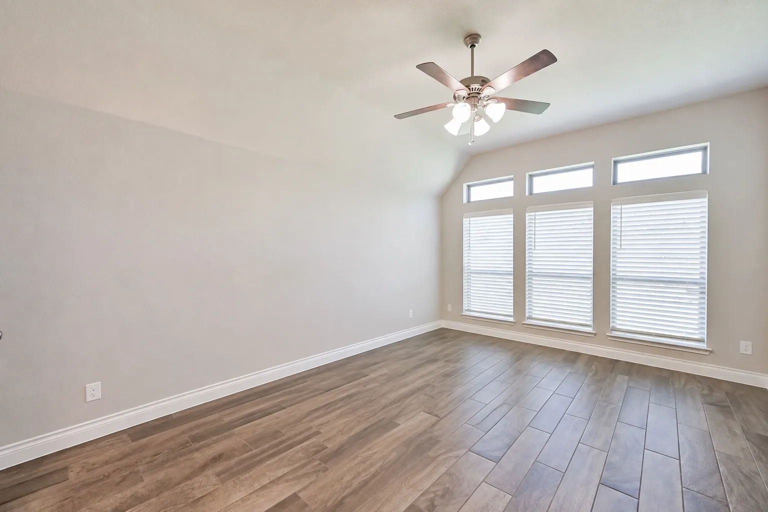 Vaulted ceiling with a ceiling fan, three windows with blinds, three transom windows, and wood-finish flooring