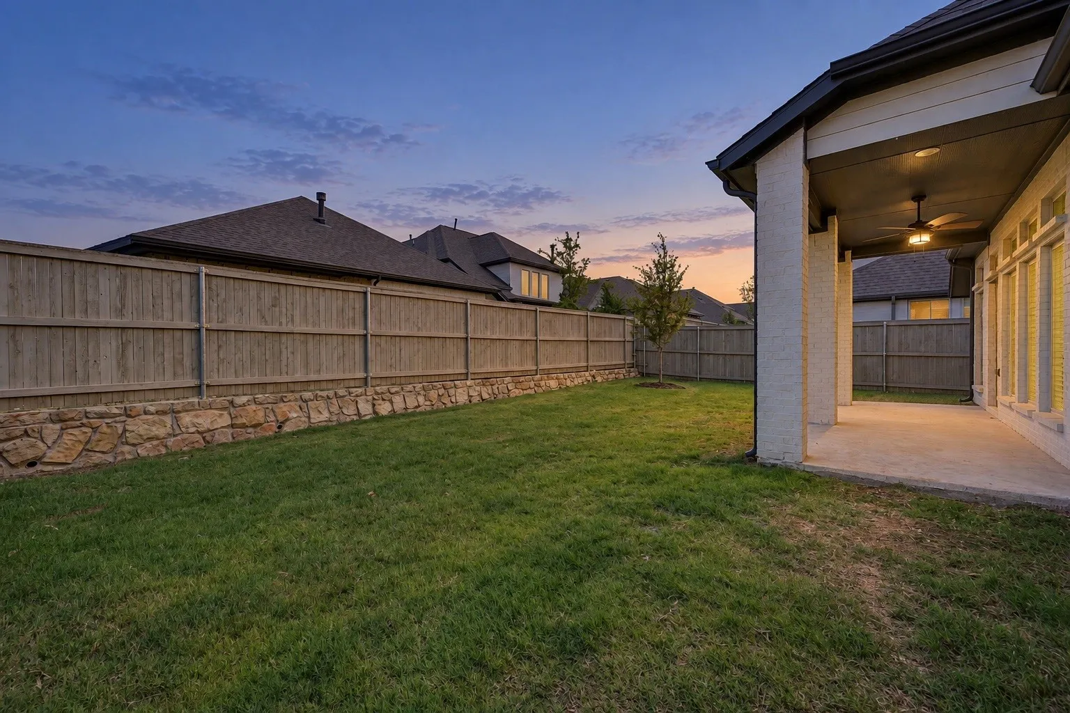 Expansive backyard featuring a manicured lawn, a wood privacy fence, and a stone retaining wall