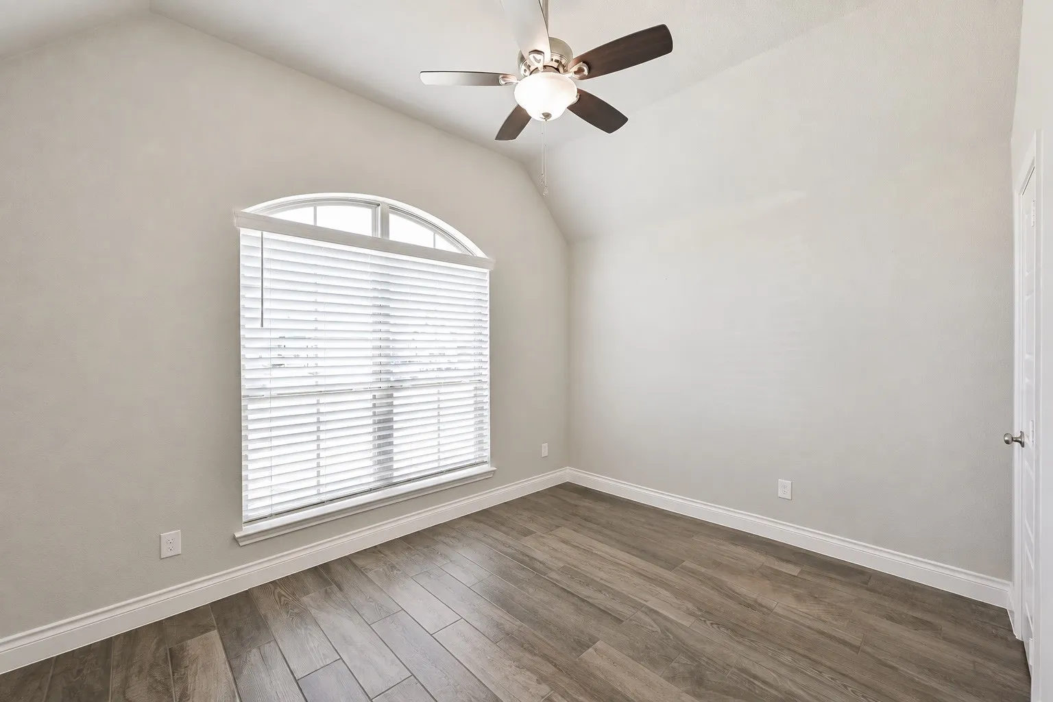 Vaulted ceiling, arched window, wood-finish flooring, ceiling fan with integrated lighting, and a paneled door