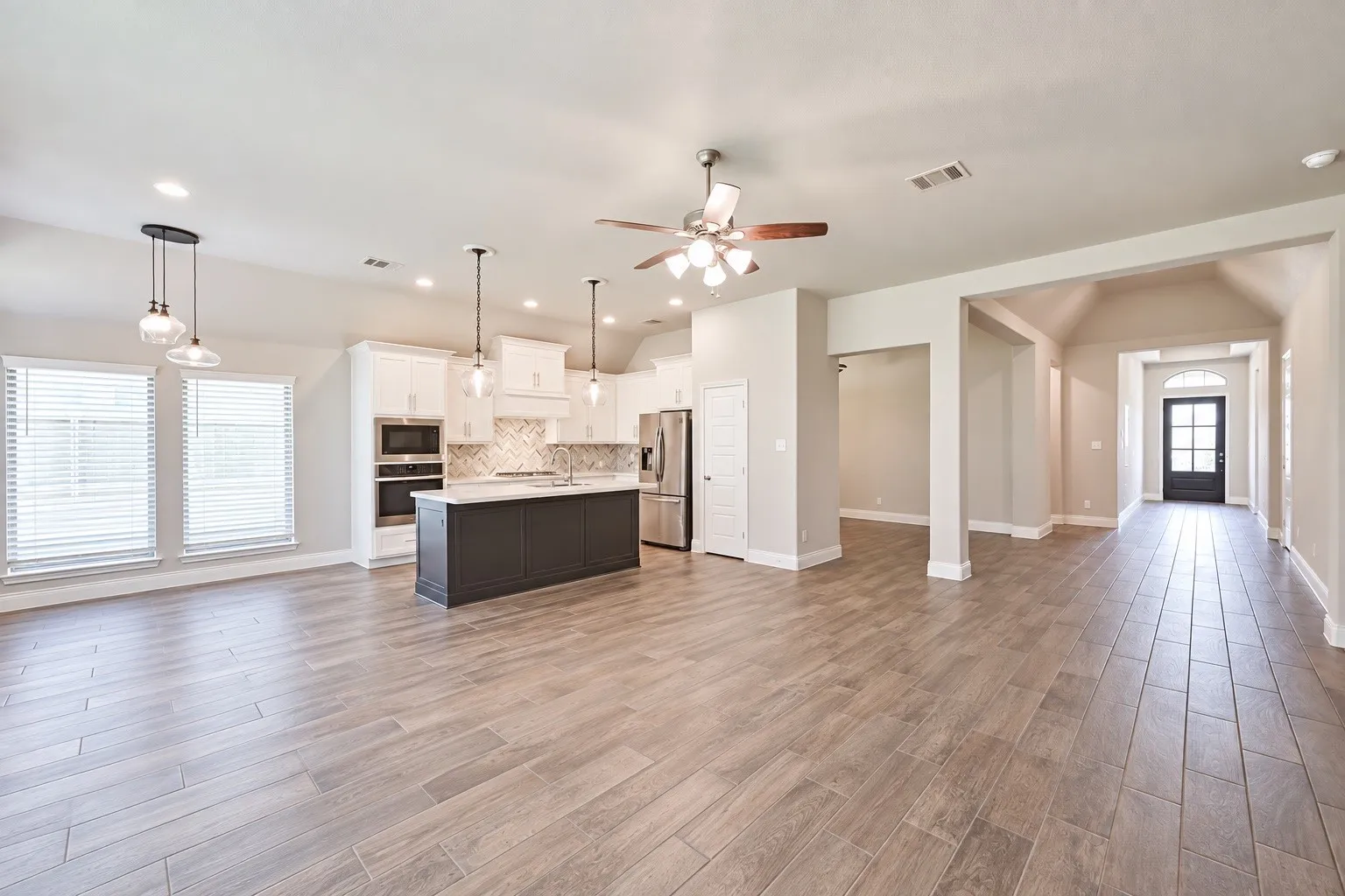 Open-concept living space featuring wood-finish tile flooring, recessed lighting, and a contemporary kitchen with a dark-toned island, pendant lights, and stainless steel appliances