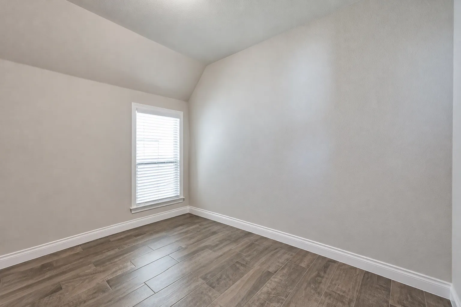 Wood-finish flooring with white trim, a single window with blinds, and neutral wall tones