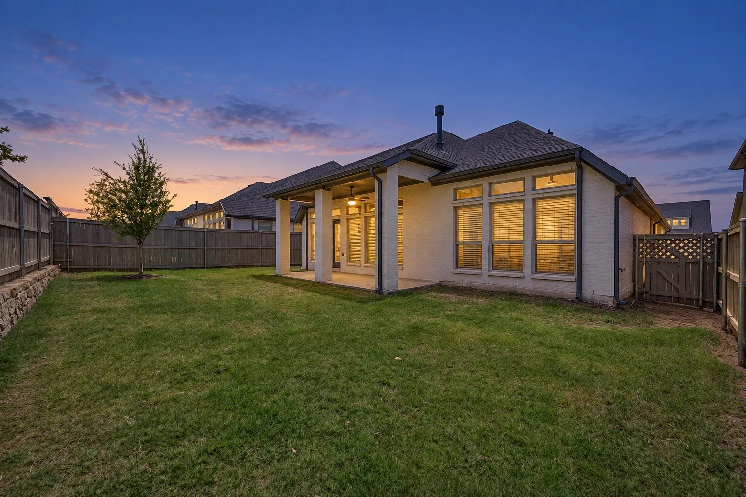 Expansive backyard with a manicured lawn, full privacy fencing, and a stone retaining wall