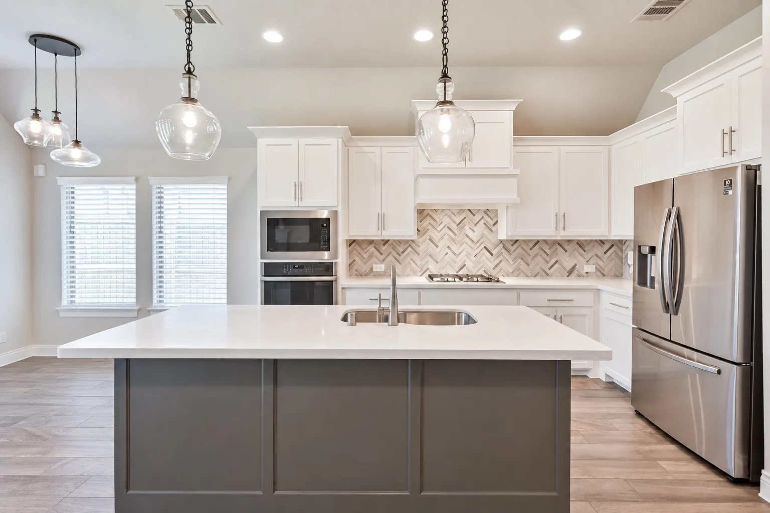 Kitchen featuring a central island with a sink, stainless steel appliances, white cabinetry, herringbone tile backsplash, and recessed lighting