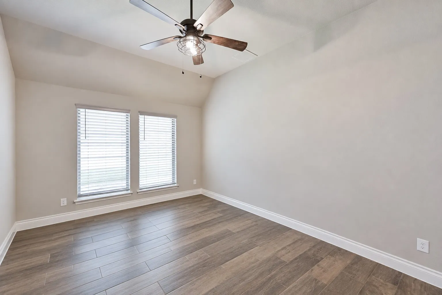 Vaulted ceiling, wood-finish flooring, dual windows with blinds, ceiling fan with integrated lighting, neutral wall tones