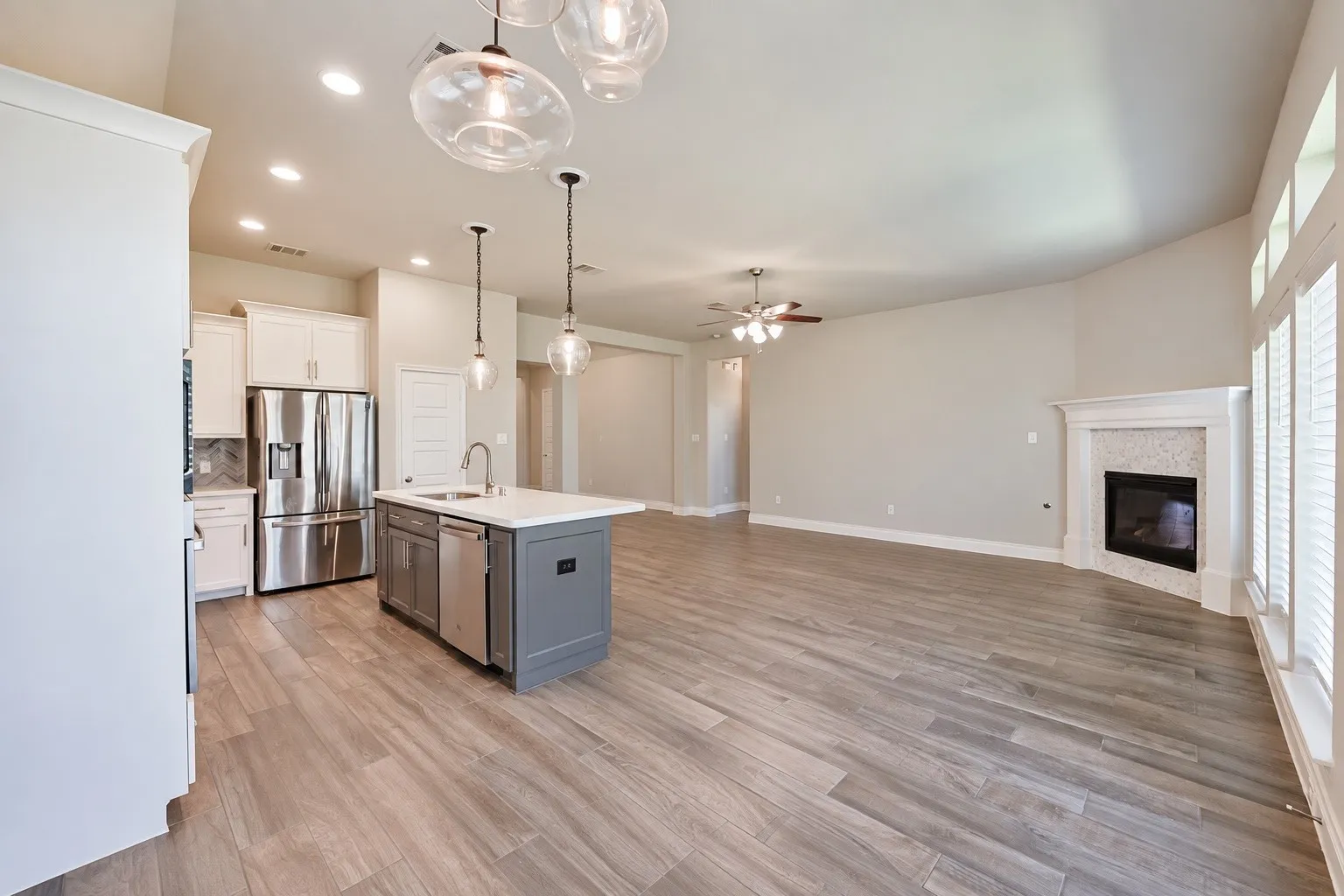 Wood-finish flooring throughout, kitchen island with built-in sink and dishwasher, recessed lighting, and a corner fireplace with a decorative mantel