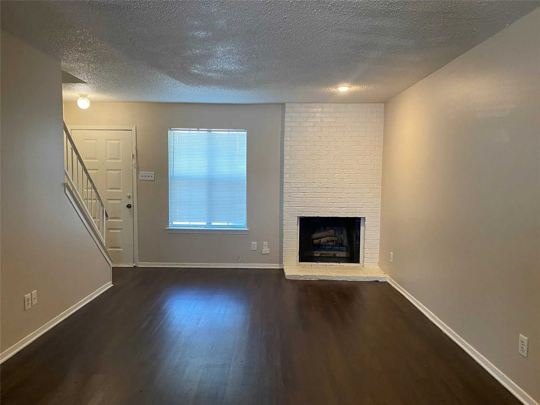 Unfurnished living room with stairway, a fireplace, baseboards, a textured ceiling, and wood finished floors