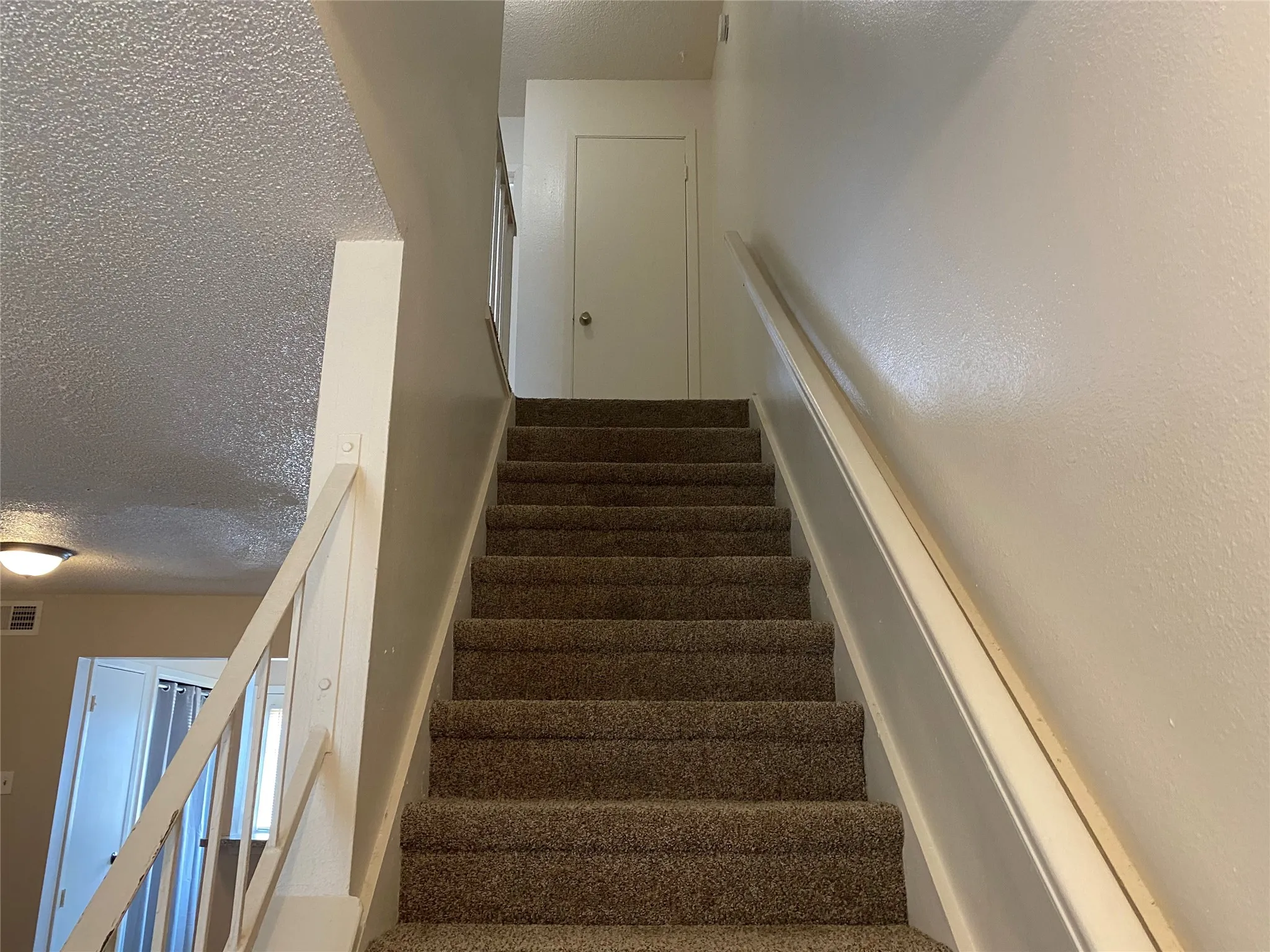 Stairs with a textured ceiling and visible vents