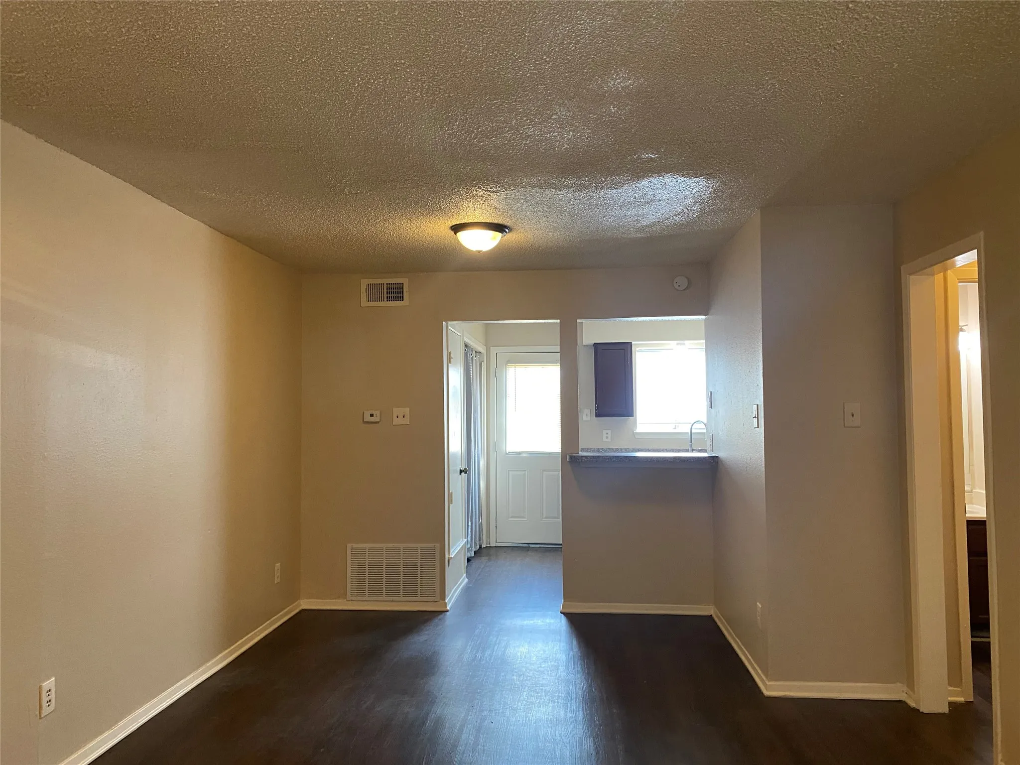 Spare room with a textured ceiling, visible vents, baseboards, and dark wood-type flooring